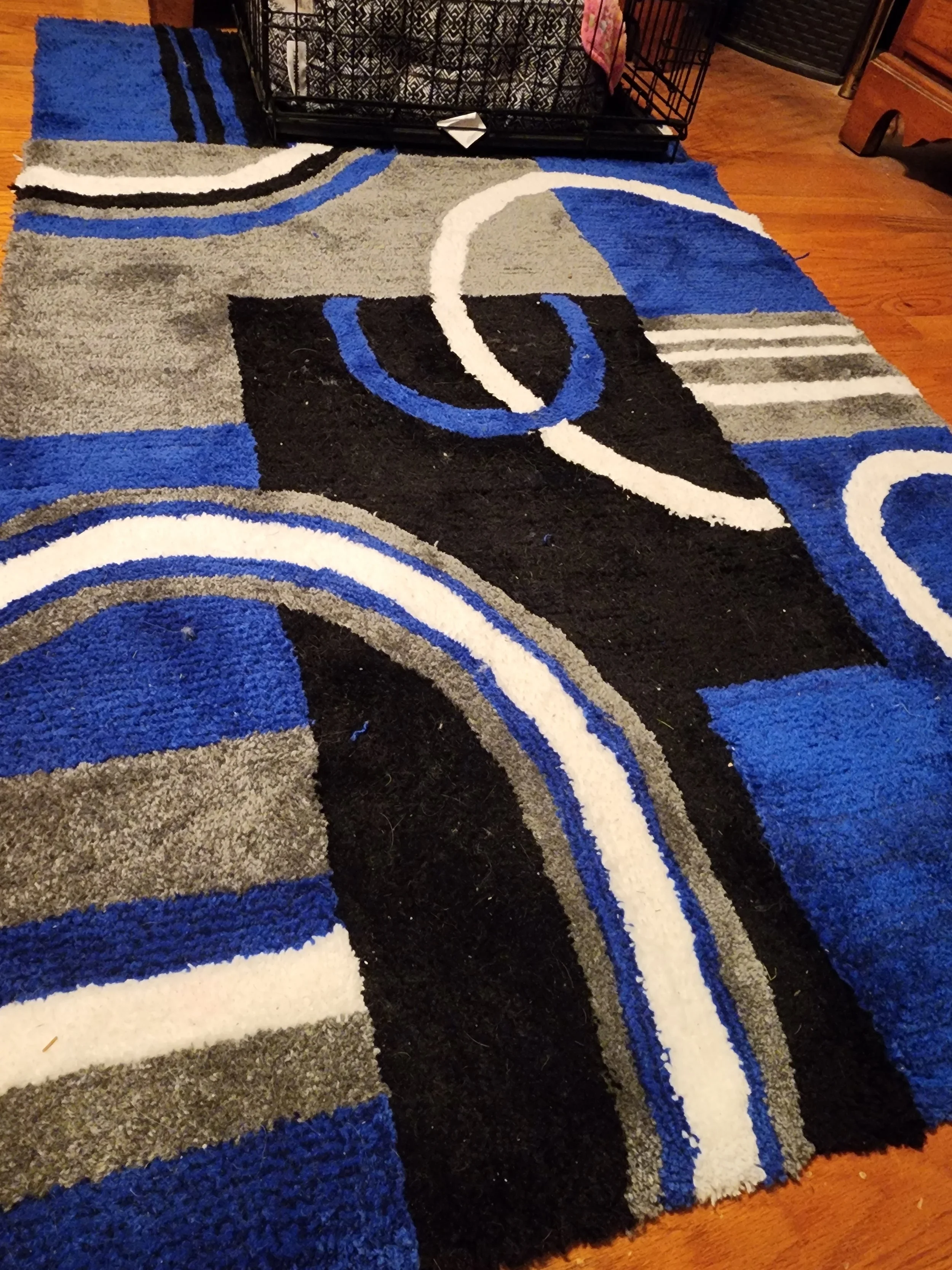 Close-up of a colorful abstract-patterned rug with shades of black, white, blue, gray, and beige, placed on a wooden floor.