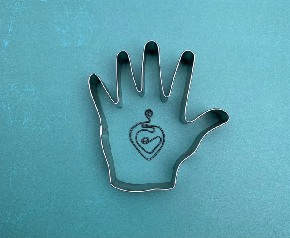 Metal hand-shaped cookie cutter with a small wire heart and swirl design inside, on a blue textured background.