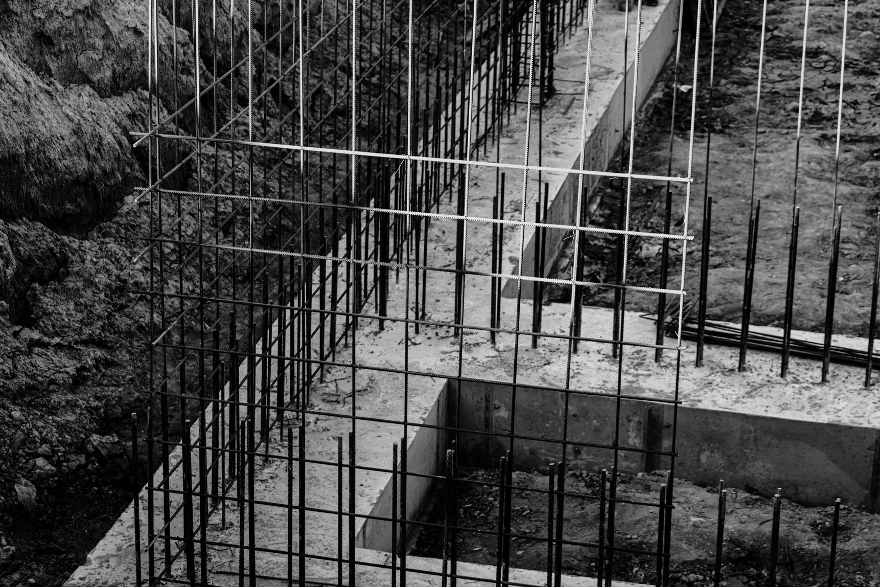 An underground construction site with steel rebar framework for future concrete walls or foundation, surrounded by dirt and gravel.