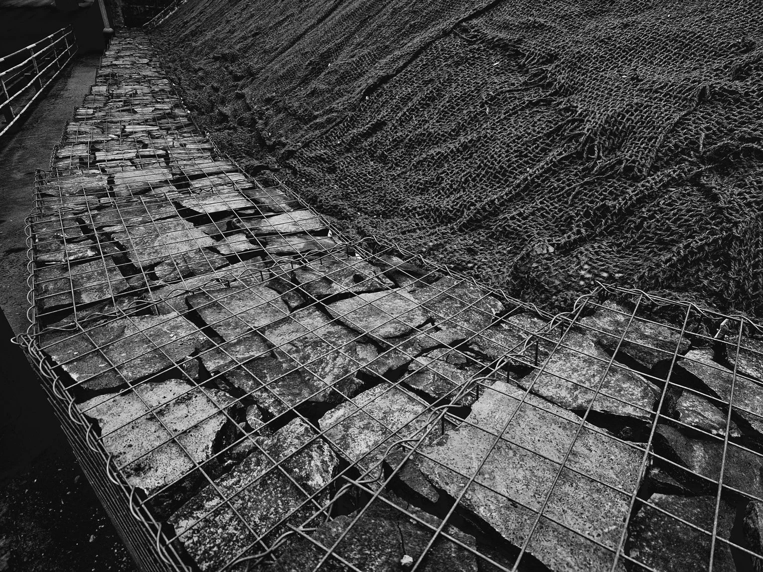 A metal wire cage filled with irregular stone pieces next to a large mound of rough-textured soil or gravel.