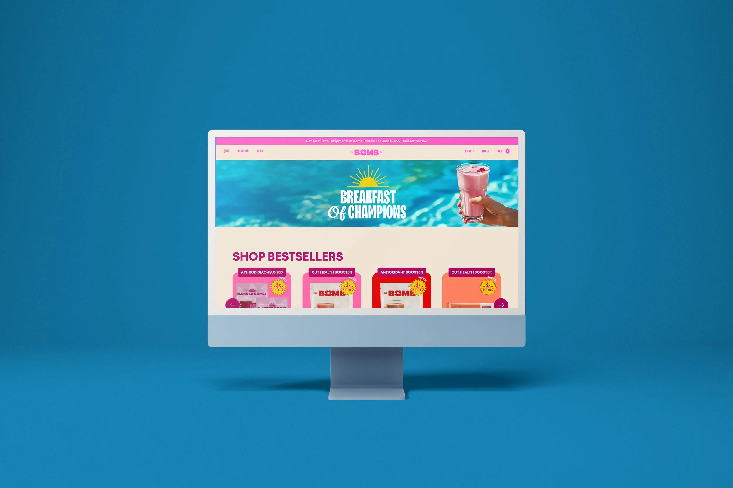 A computer monitor displays a colorful website for a health supplement brand, featuring a poolside background with a hand holding a pink smoothie and a section titled 'Breakfast of Champions' along with products labeled 'Shop Bestsellers.'