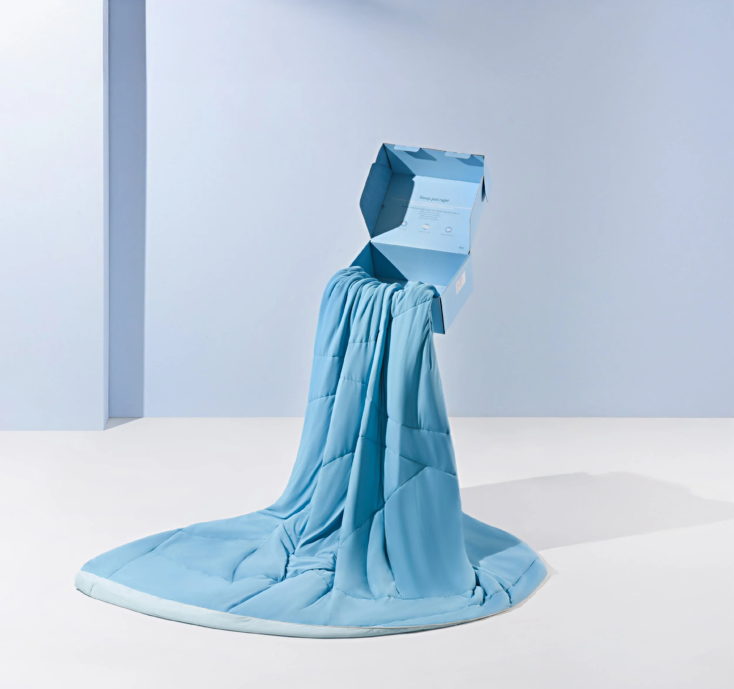 A blue quilted comforter draped over a box, with the box suspended in the air against a pale blue background.