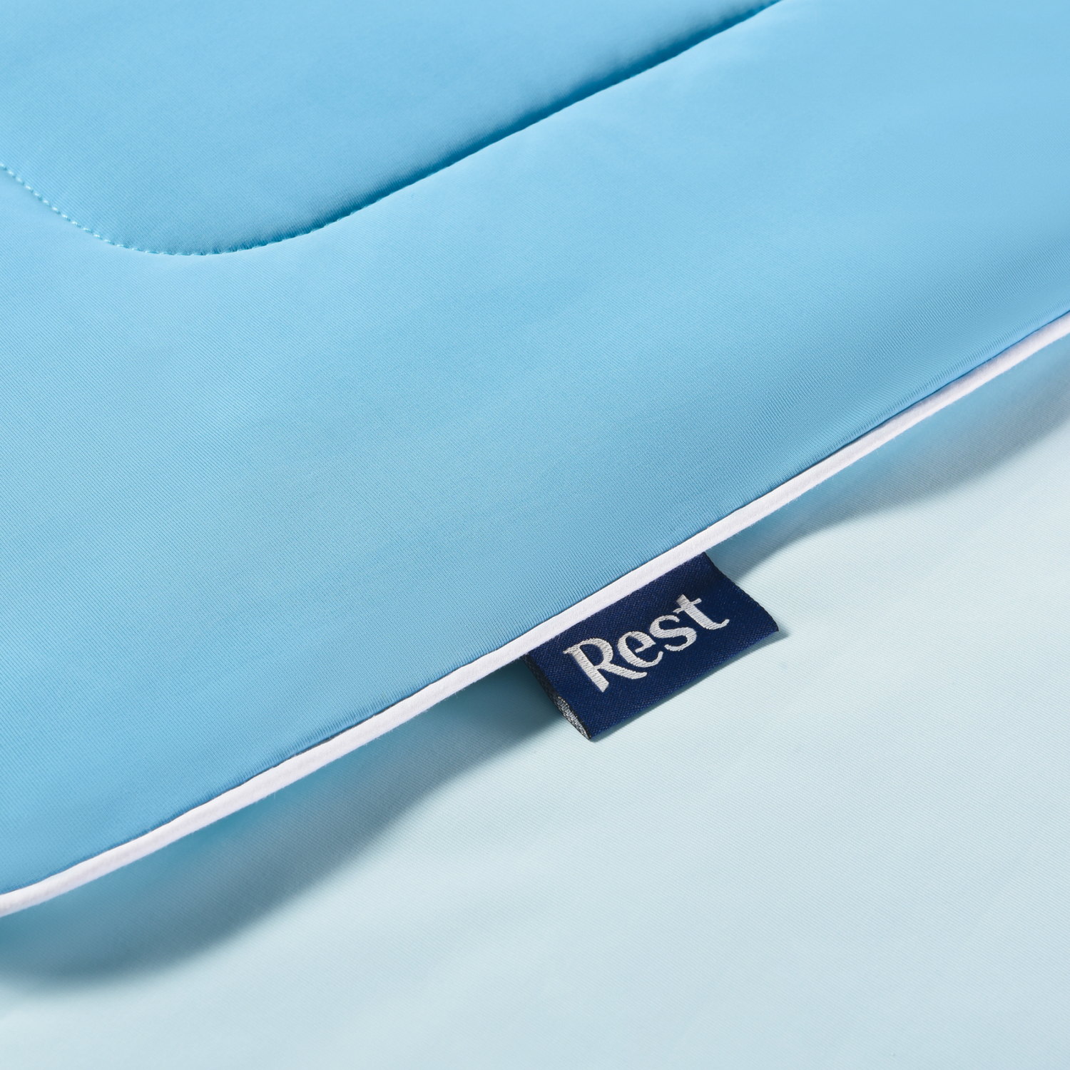 Close-up of a blue mattress with a small navy blue tag labeled 'Rest' attached to the edge.
