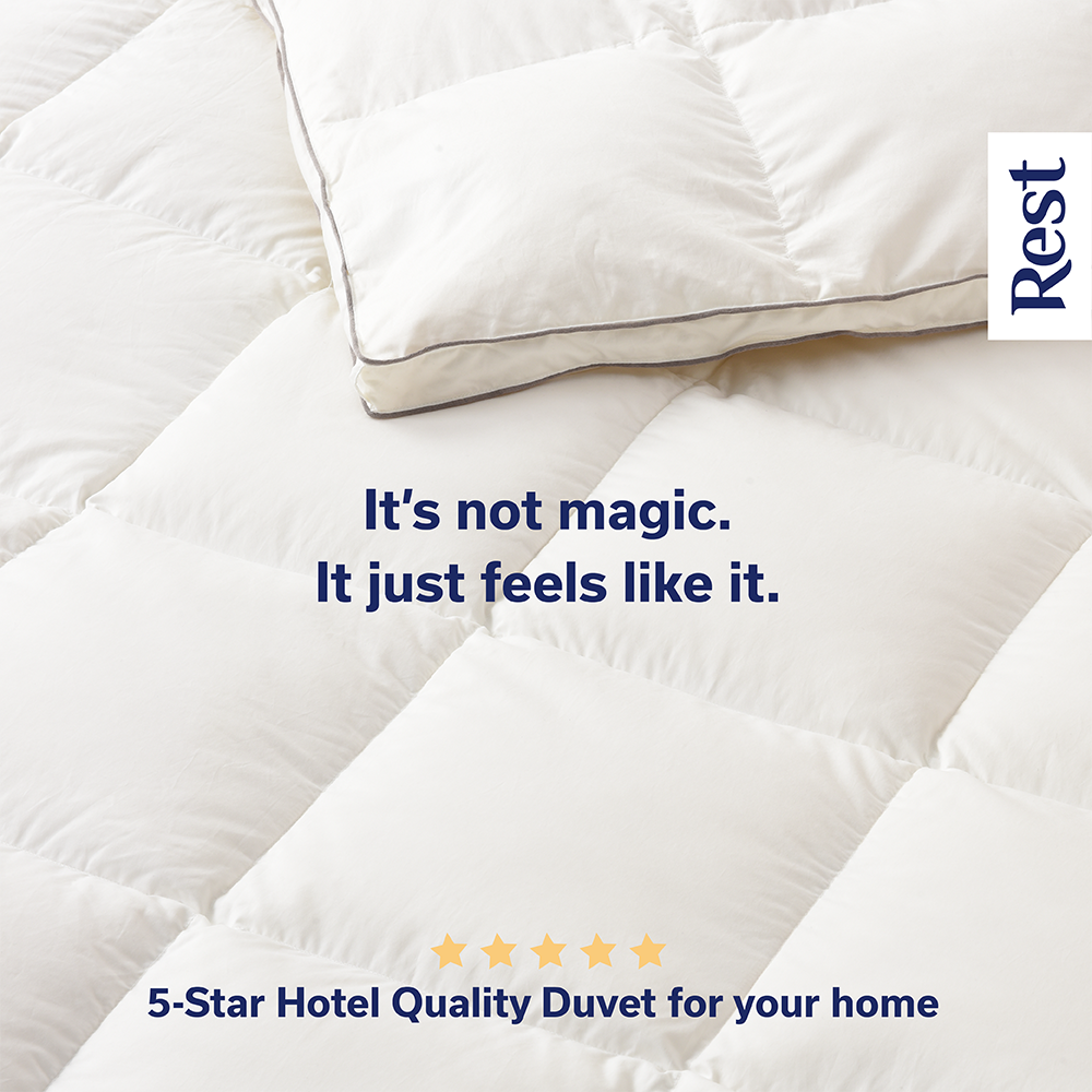 A white, plush comforter and pillow on a bed, with text overlay that says, "It's not magic. It just feels like it." and "5-Star Hotel Quality Duvet for your home", and a small white label in the top right corner with the word, "Rest".