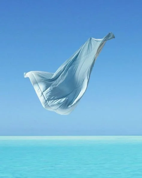 A white cloth or sheet floating in the air above a body of water with a clear blue sky in the background.