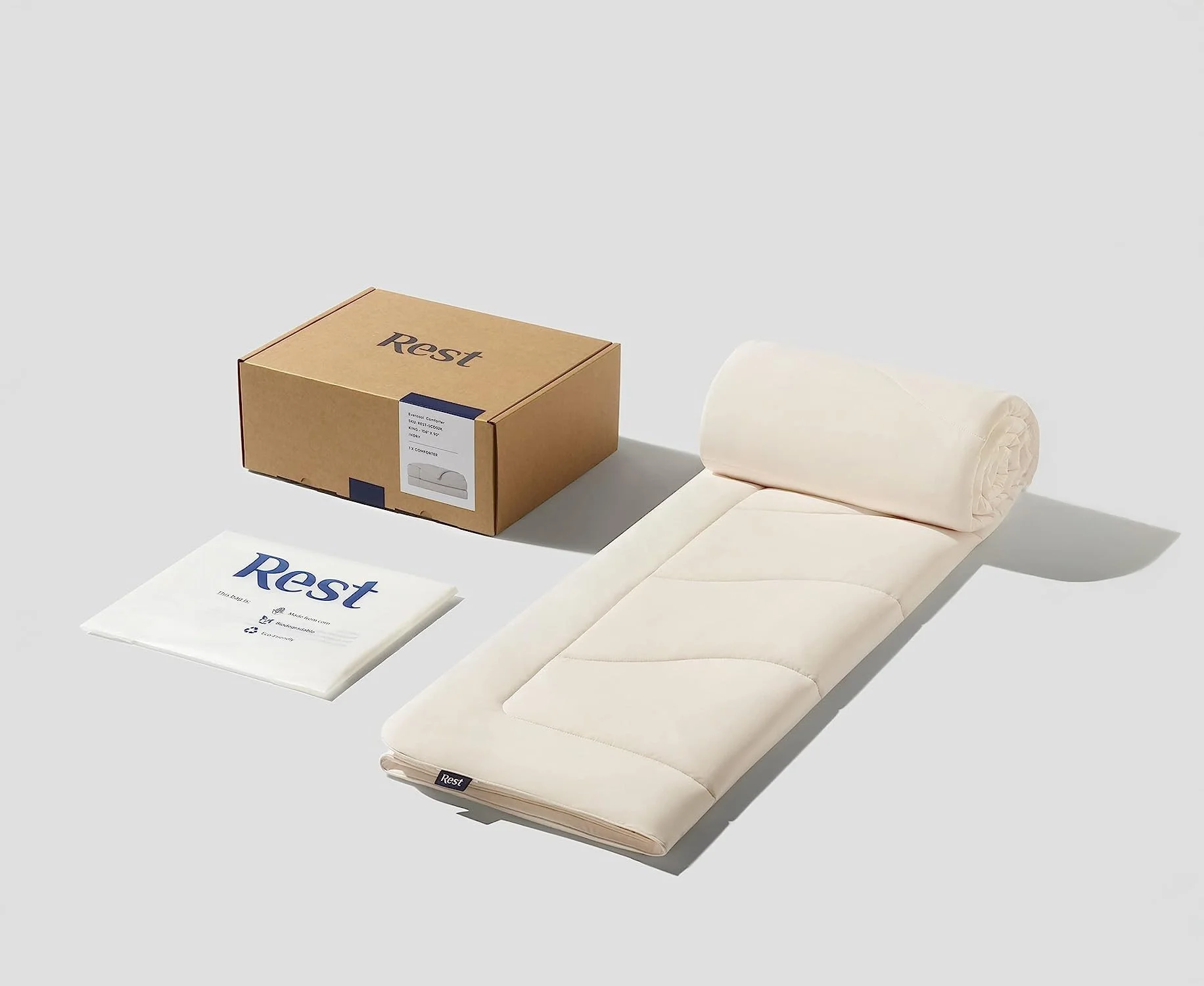A beige medical mattress with a cylindrical pillow, a box labeled 'Rest,' and a plastic-wrapped sheet labeled 'Rest' on a light gray background.
