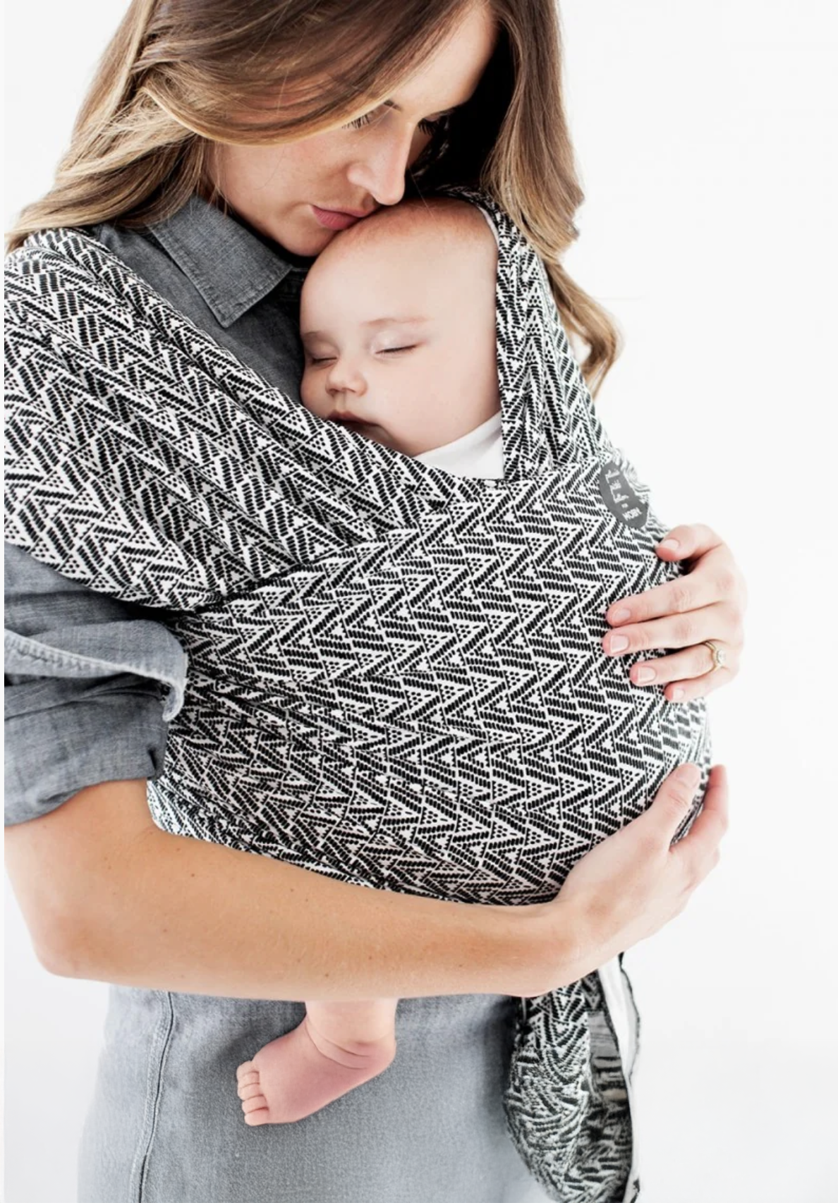 A woman holding a sleeping baby close to her chest in a patterned sling.
