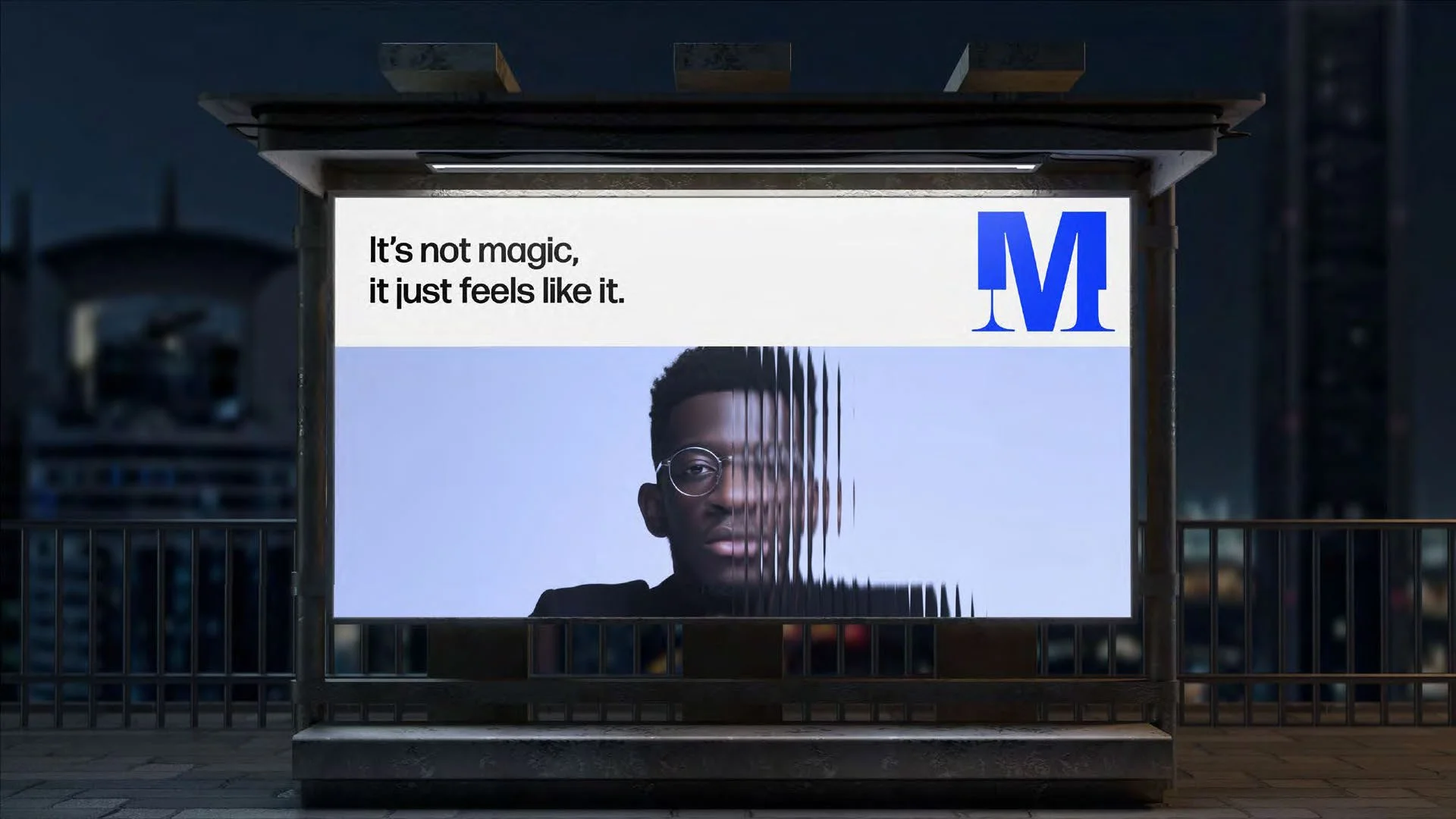 A bus stop advertisement featuring a man with short black hair and glasses, with a distorted right half of his face. The ad text reads, "It's not magic, it just feels like it," with a blue *M* logo in the top right corner. The background shows a cityscape at night.