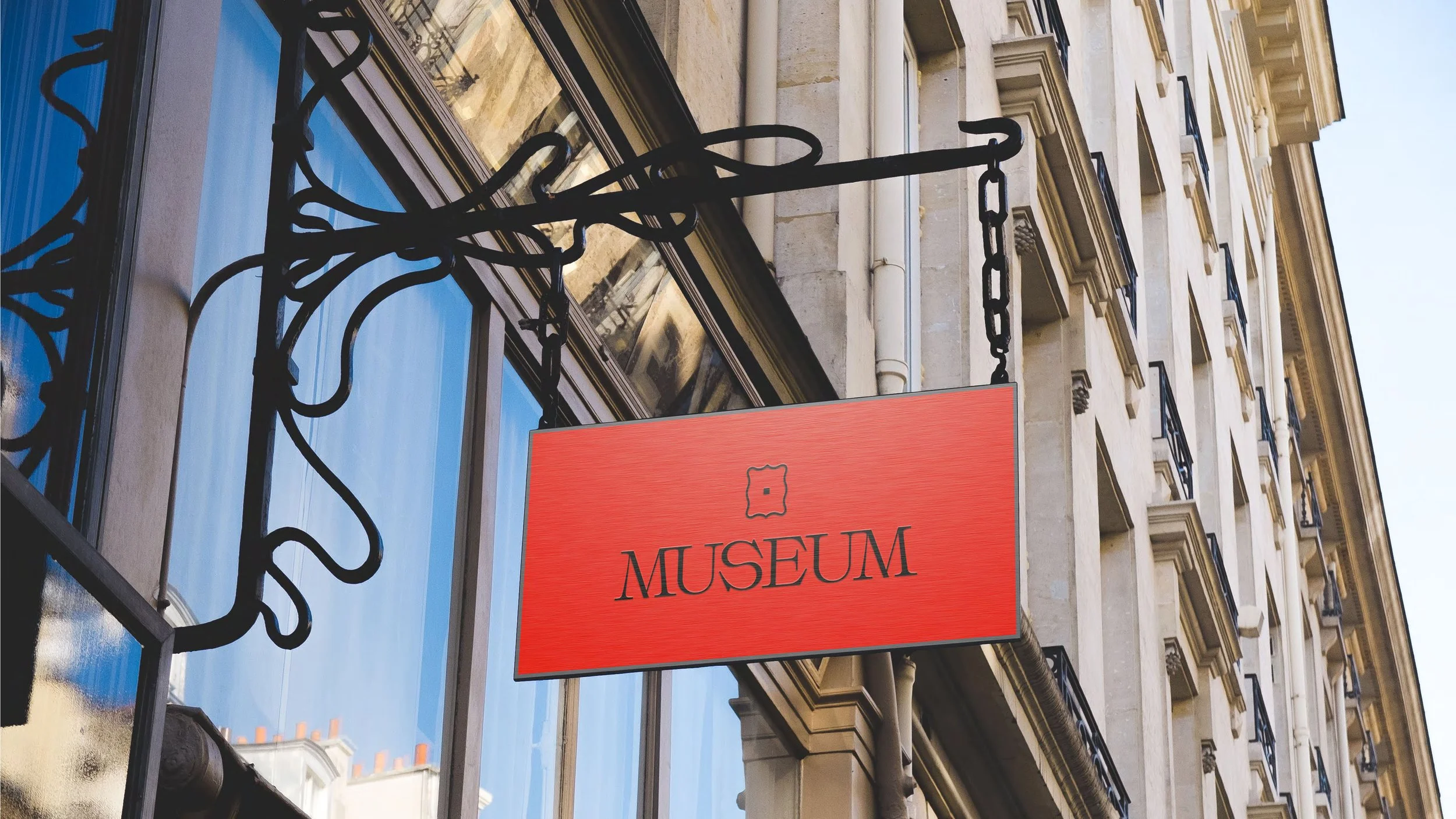 Red museum sign hanging outside a building with ornate window frames and balconies.