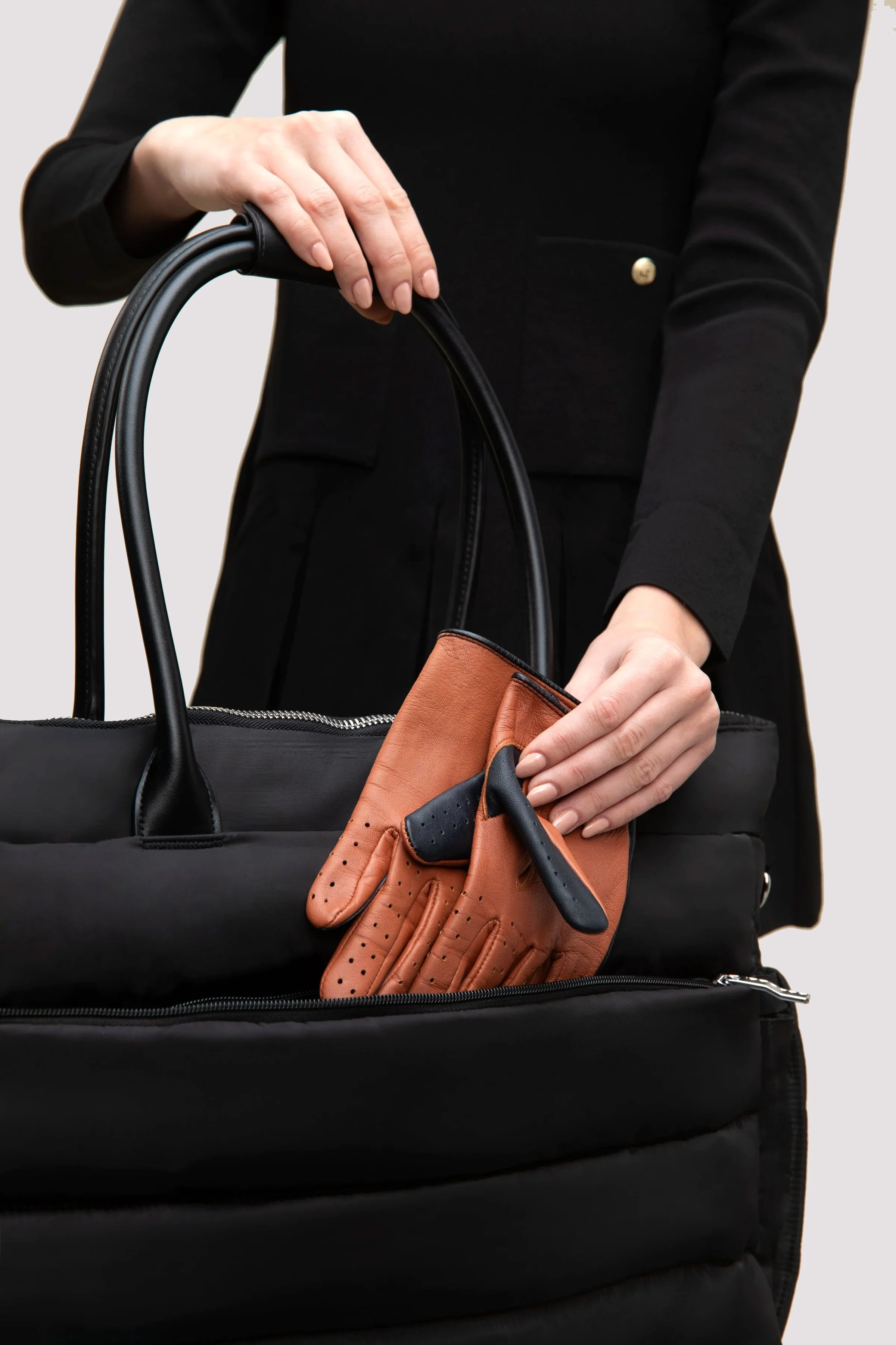A person in black clothing placing brown and black gloves into a black handbag.