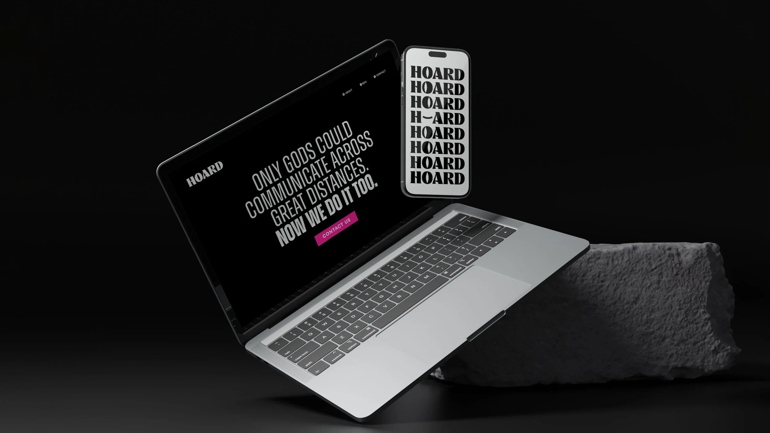 A laptop and a smartphone display with the word 'HOARD' repeated and a message about communication during great distances, placed on a rock against a black background.
