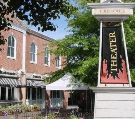 Exterior of a theater with a sign reading 'Theater' and a tent outside, opposite a brick building with multiple windows.