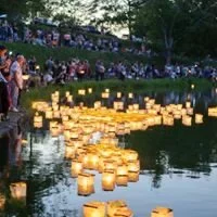 People release floating lanterns on a body of water during dusk.