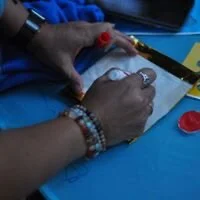 Person using a glue gun to attach a small object to a package or box on a blue surface.