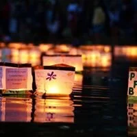 Floating candles on water during evening with illuminated paper lanterns in the background