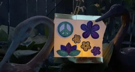 A colorful sign with peace symbols and flowers, held by gloved hands.