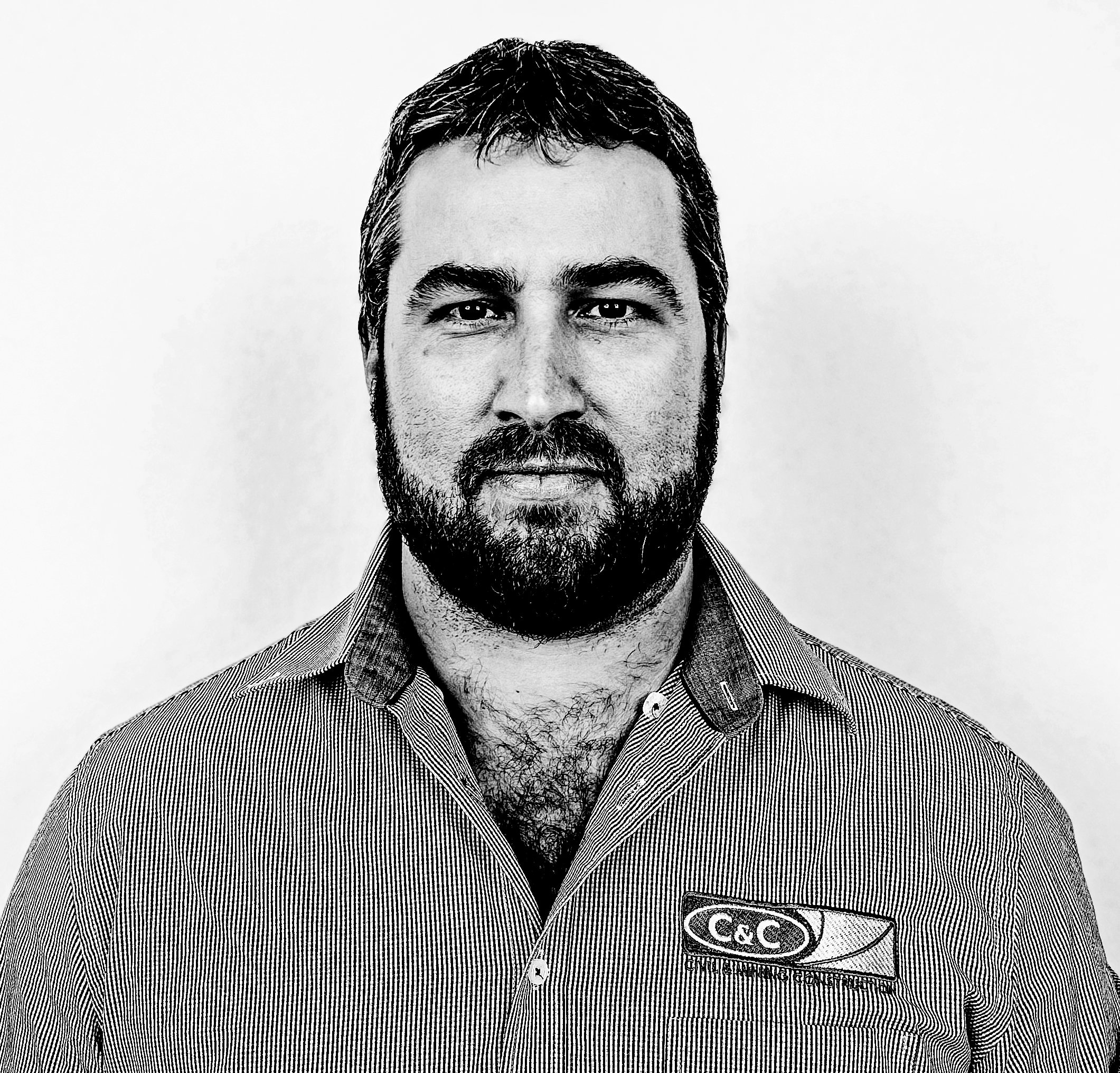 A black and white portrait of a man with short dark hair, a beard, and mustache, wearing a collared shirt with an 'Coca-Cola' logo patch.