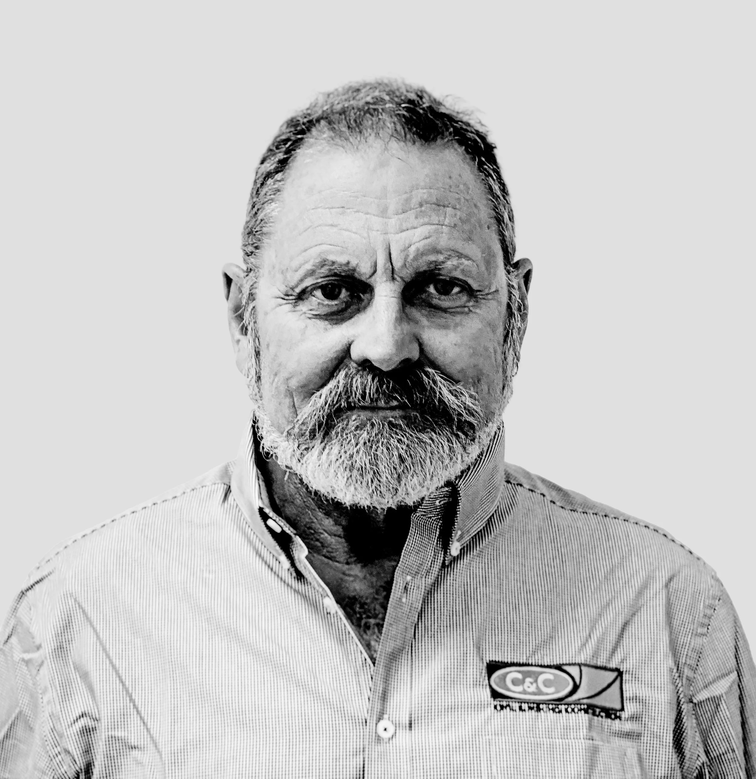 Black and white portrait of a man with a beard wearing a collared shirt with a logo on the chest, smiling slightly.