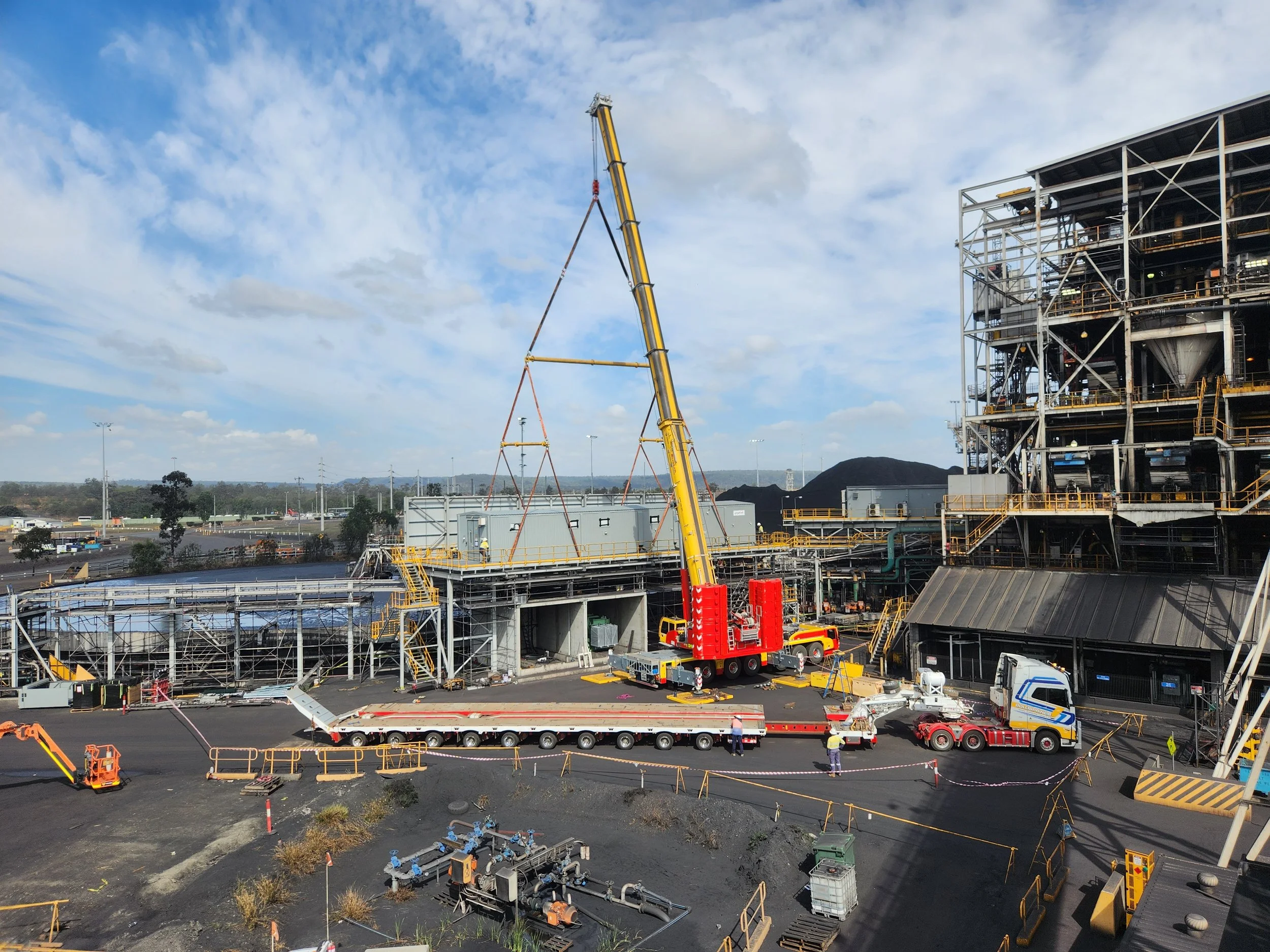 Construction site with scaffolding, equipment, and trucks under a partly cloudy sky.