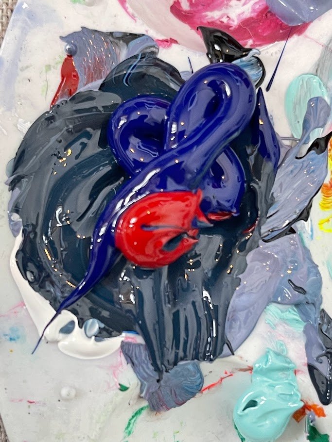 Close-up of a mixed palette of oil or acrylic paints with dark gray, purple, and red colors, with some spots of white, green, and yellow.