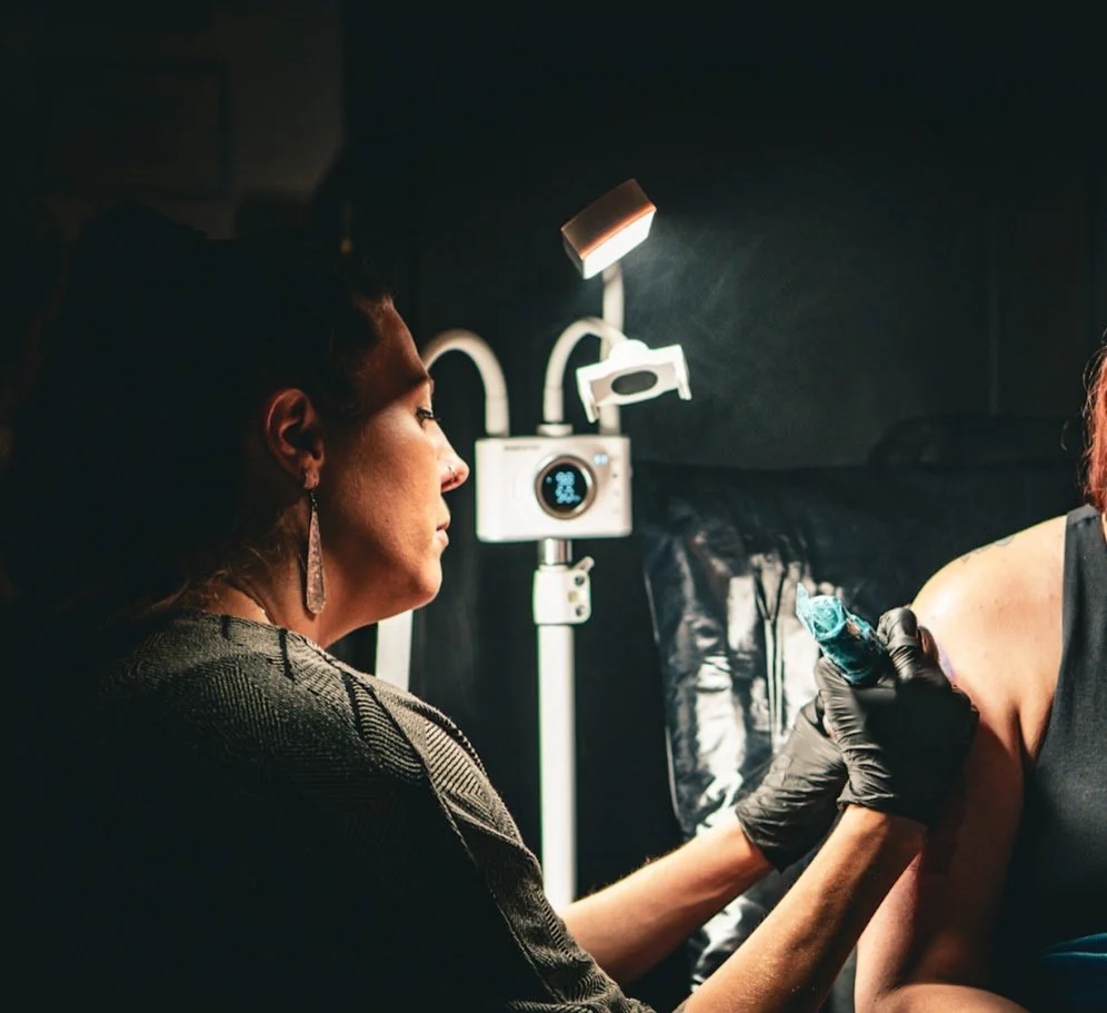 Alicia Maye tattooing a client at Inklinations private tattoo studio in a dimly lit setting, Cashmere WA.