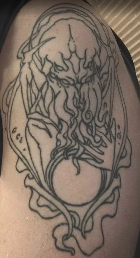 Line art tattoo of a mythical creature resembling a dragon or serpent with intricate details, including flowing lines and a circular element at the bottom.