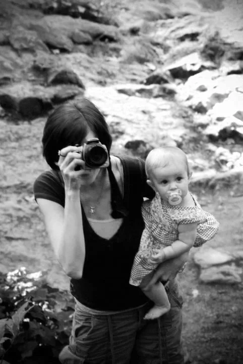 Alicia Maye photographing outdoors while holding baby daughter Fierah. The beginning of her photography career.