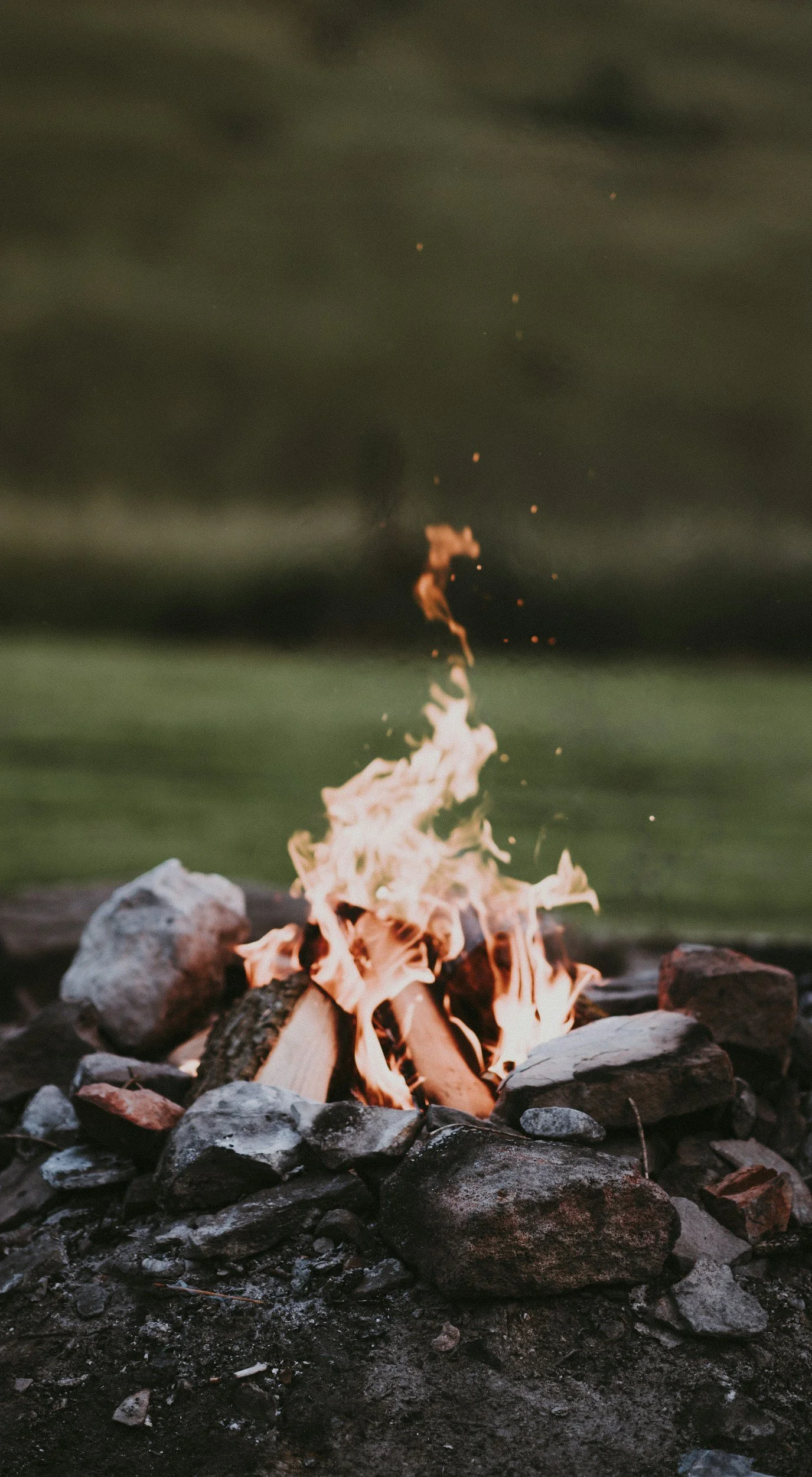 A small campfire with flames burning among rocks on a dark, possibly outdoor setting.