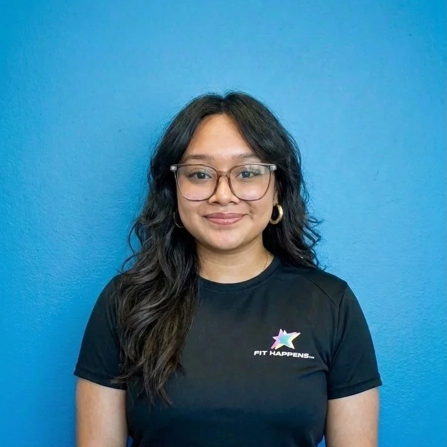 A woman with long dark hair, glasses, and earrings, smiling in front of a black brick wall.