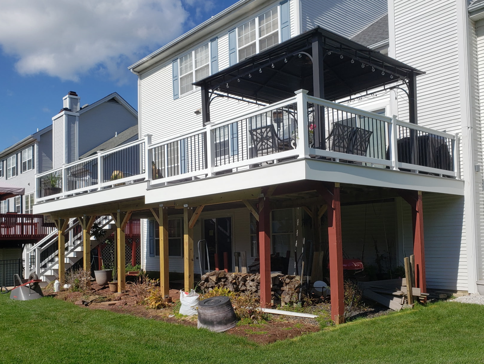A residential house with a second-floor balcony, deck with outdoor furniture, and a garden below with tools and supplies.