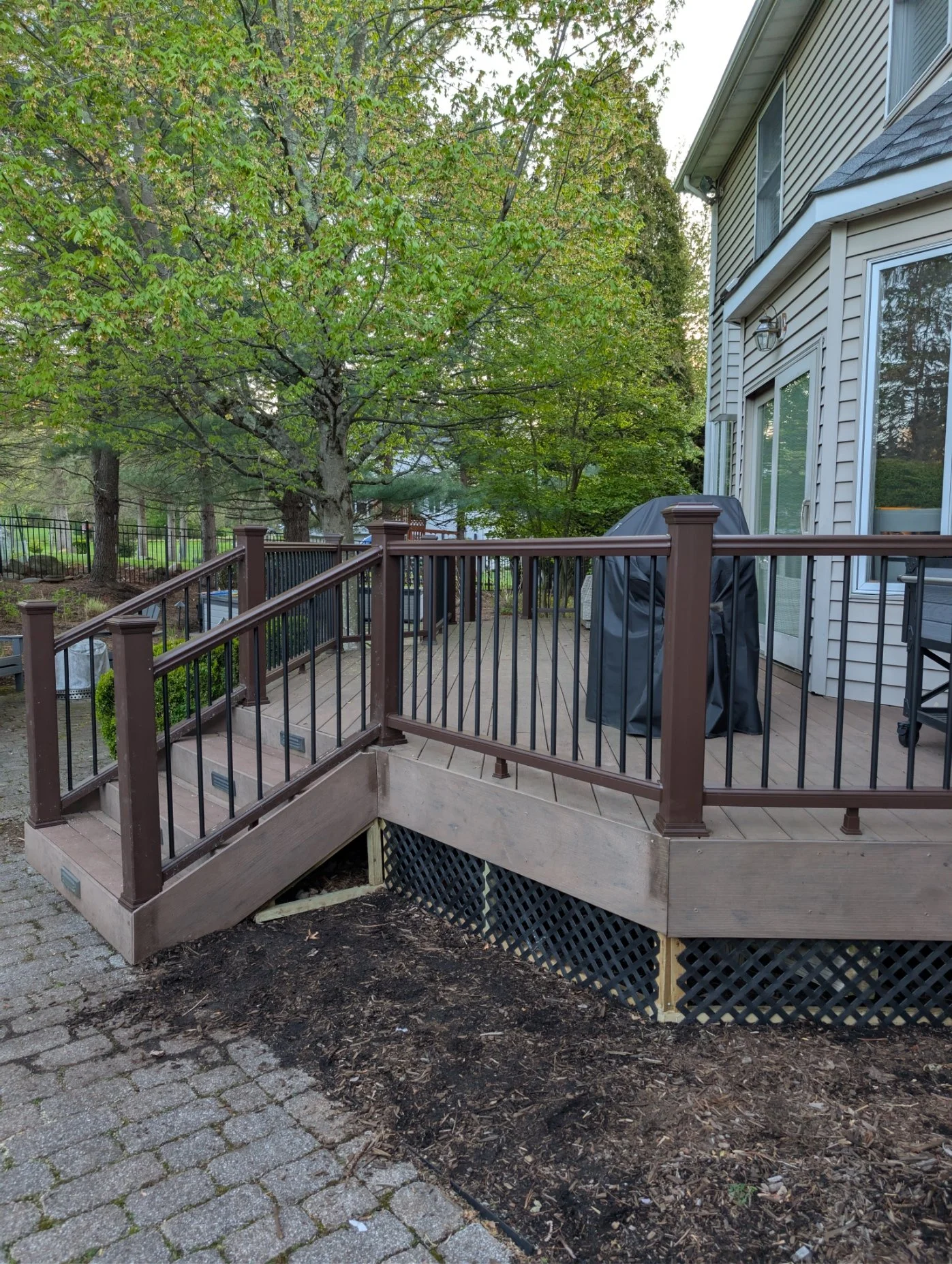A wooden deck with metal railings attached to a house, surrounded by trees with green leaves.