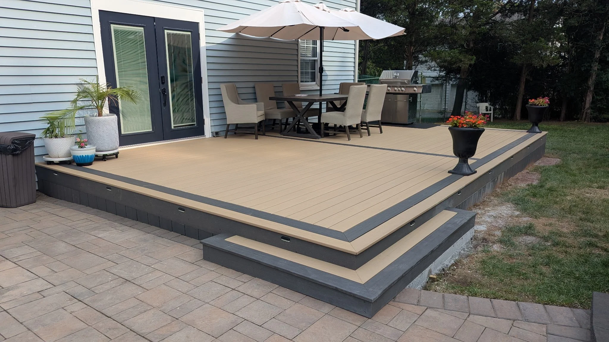 Special designed deck with stairs, outdoor dining table with umbrella, potted plants, and barbecue grill in backyard.