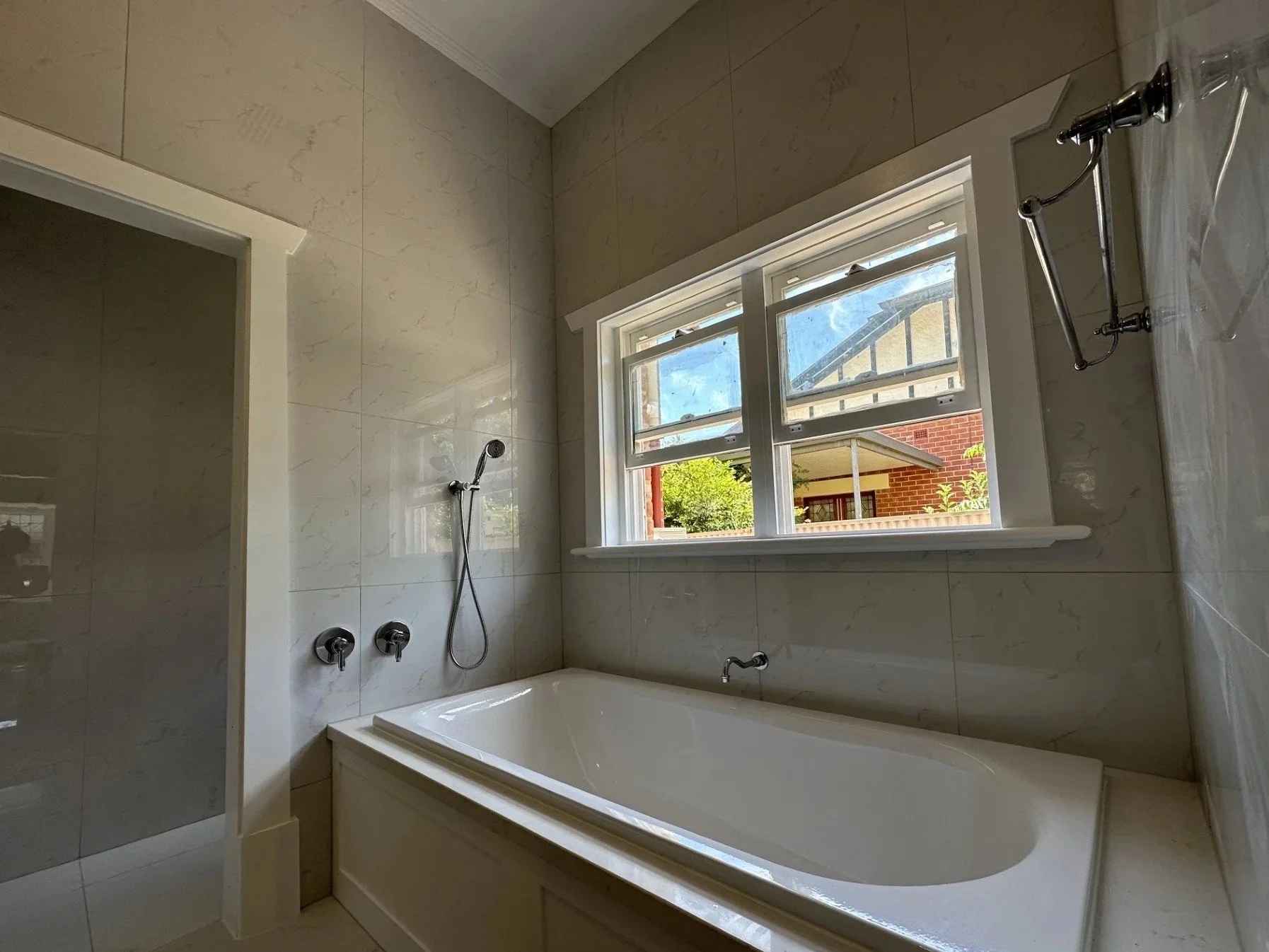 Bathroom with a large window, bathtub, and handheld shower.