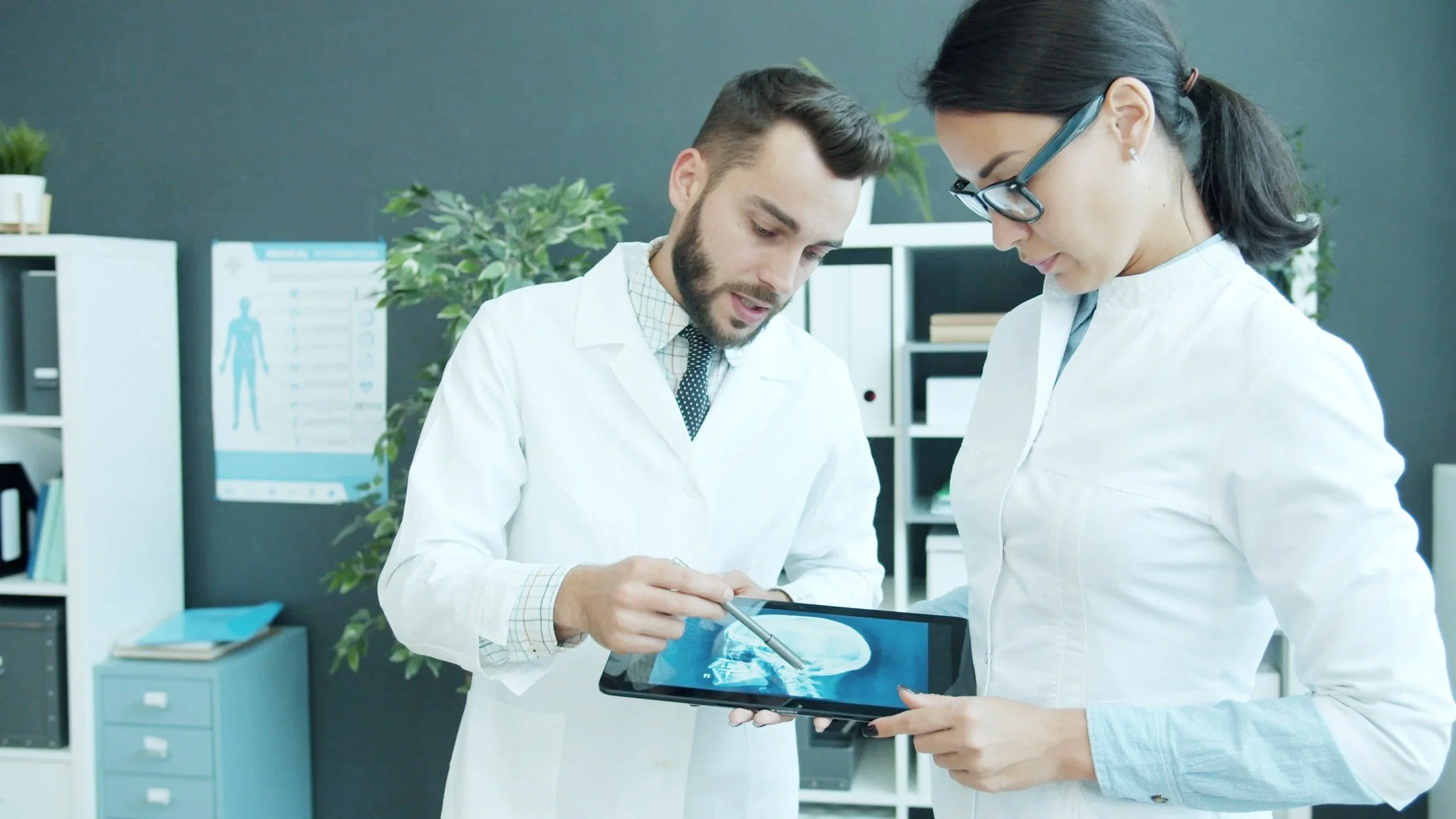 Two scientists, a man with a beard and a woman with glasses, examining an X-ray on a tablet in a laboratory.