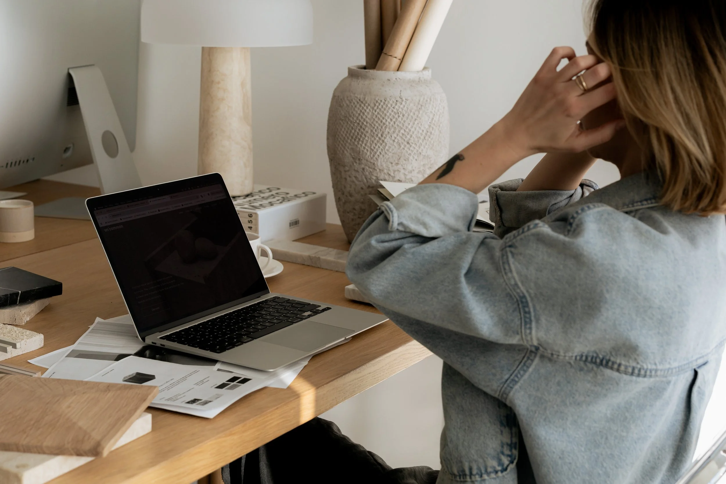 A business leader sitting at a desk with an open laptop and paperwork, looking overwhelmed.