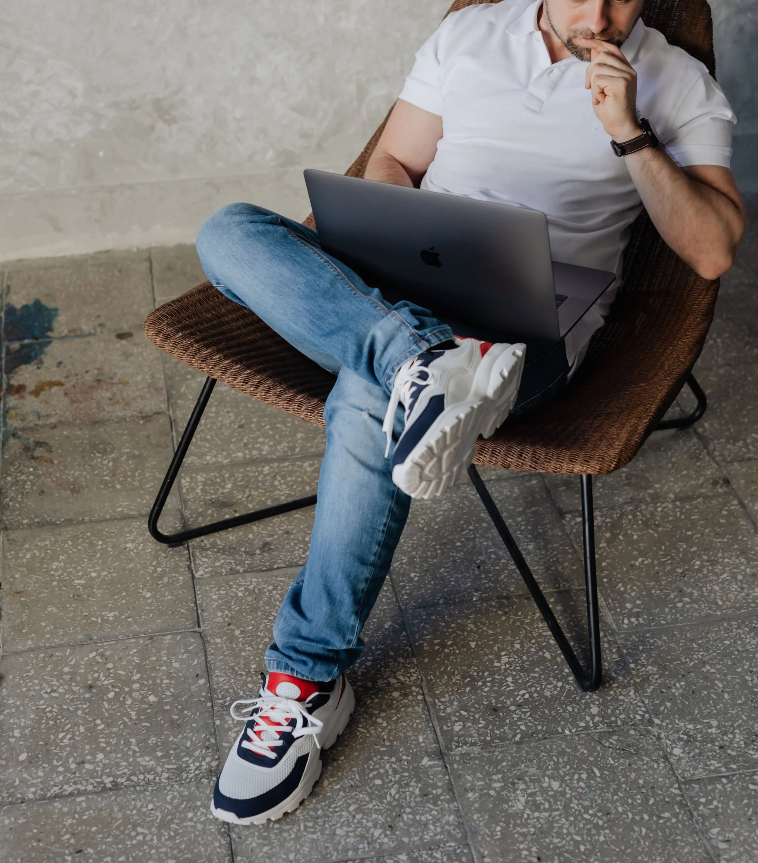 A young professional thinking, sitting in a chair while working on a laptop.
