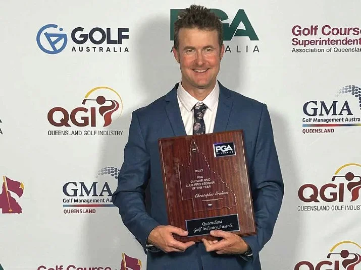 A man in a blue suit holding a wooden award plaque with the PGA Australia logo, standing in front of a backdrop featuring logos of Golf Australia, Queensland Golf Industry, and Golf Management Australia.