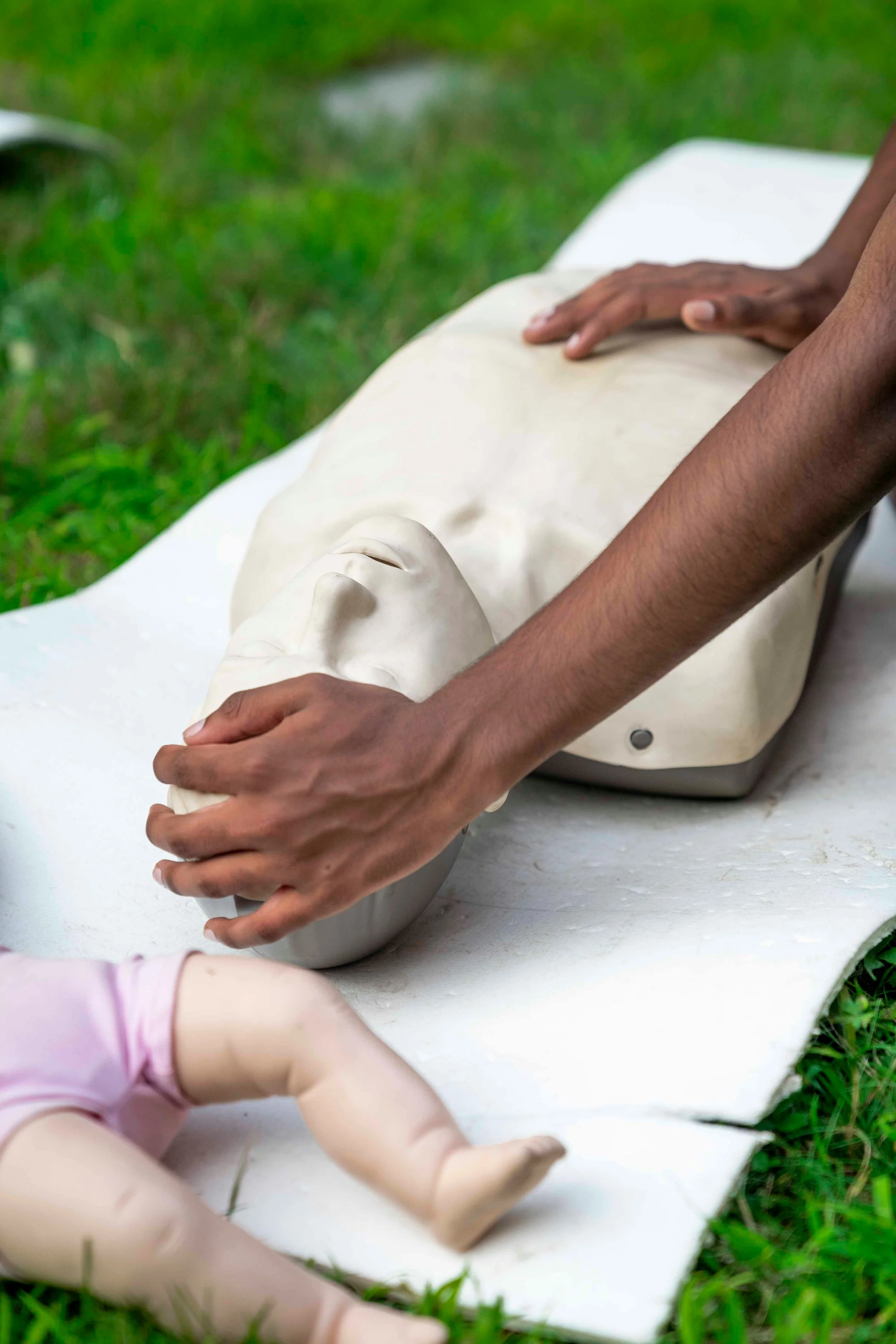 Person performing CPR on a mannequin outdoors on the grass