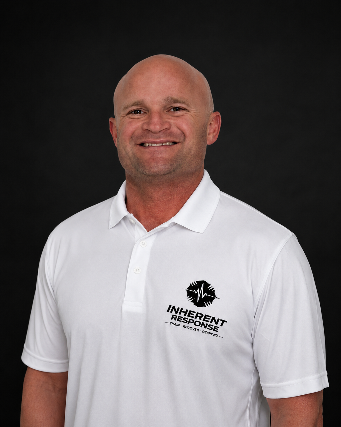 Portrait of a smiling man wearing a white polo shirt with a logo that says "Inherent Response" and "Train - Recover - Respond" on a black background.