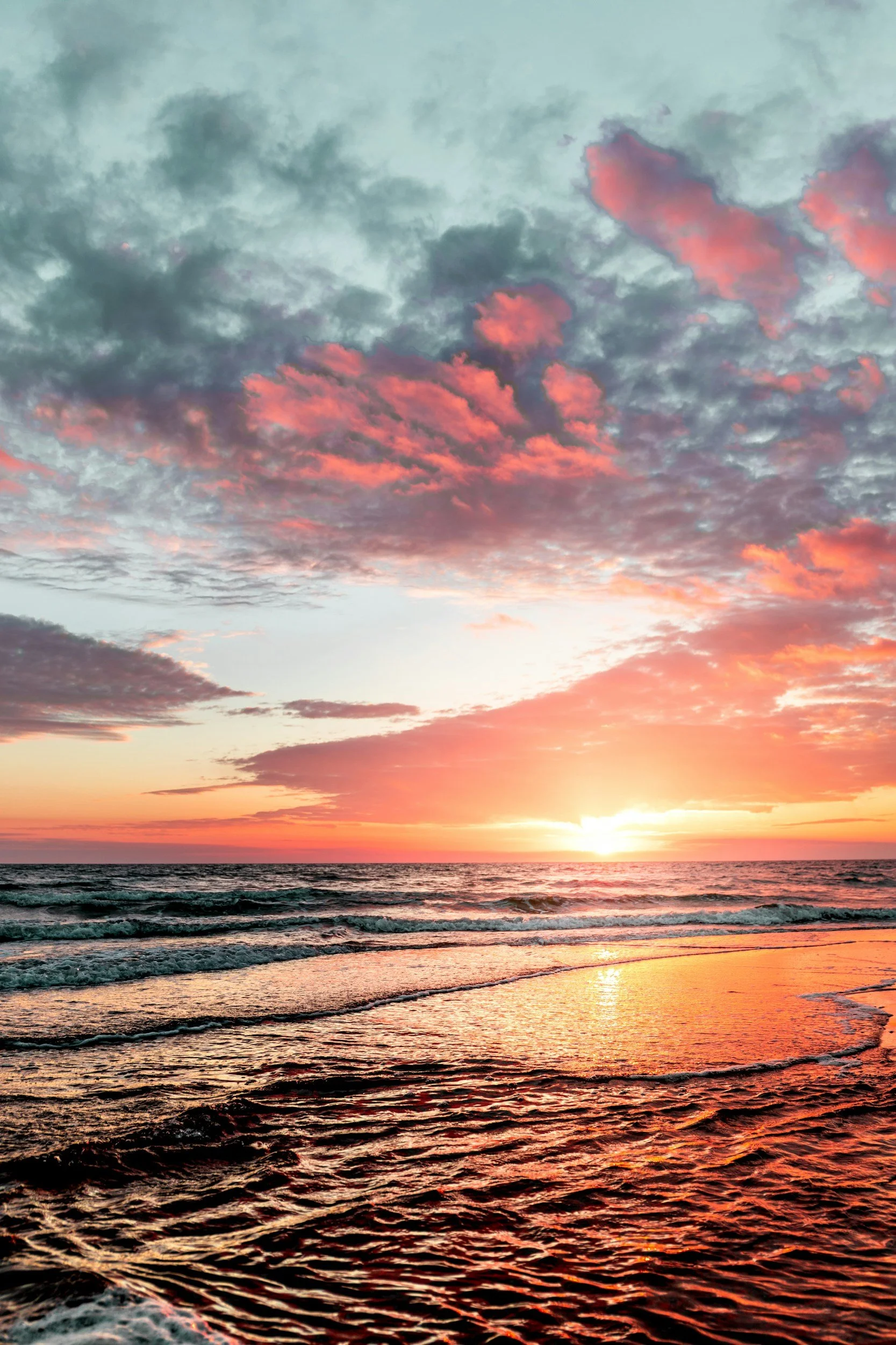 A sunset over the ocean with pink and orange clouds in the sky and waves on the water.
