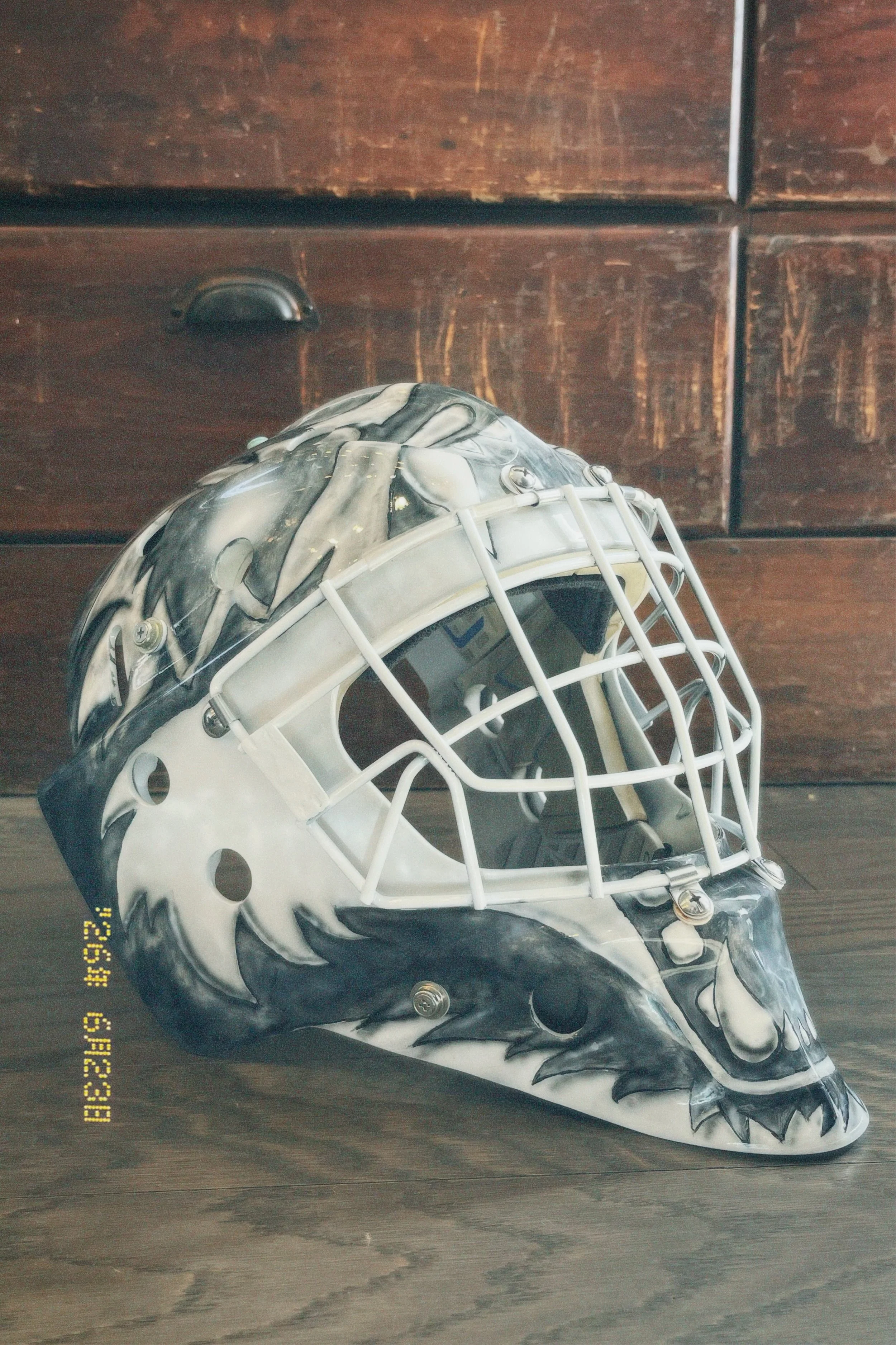 A hockey goalie mask with an eagle design on a wooden surface.