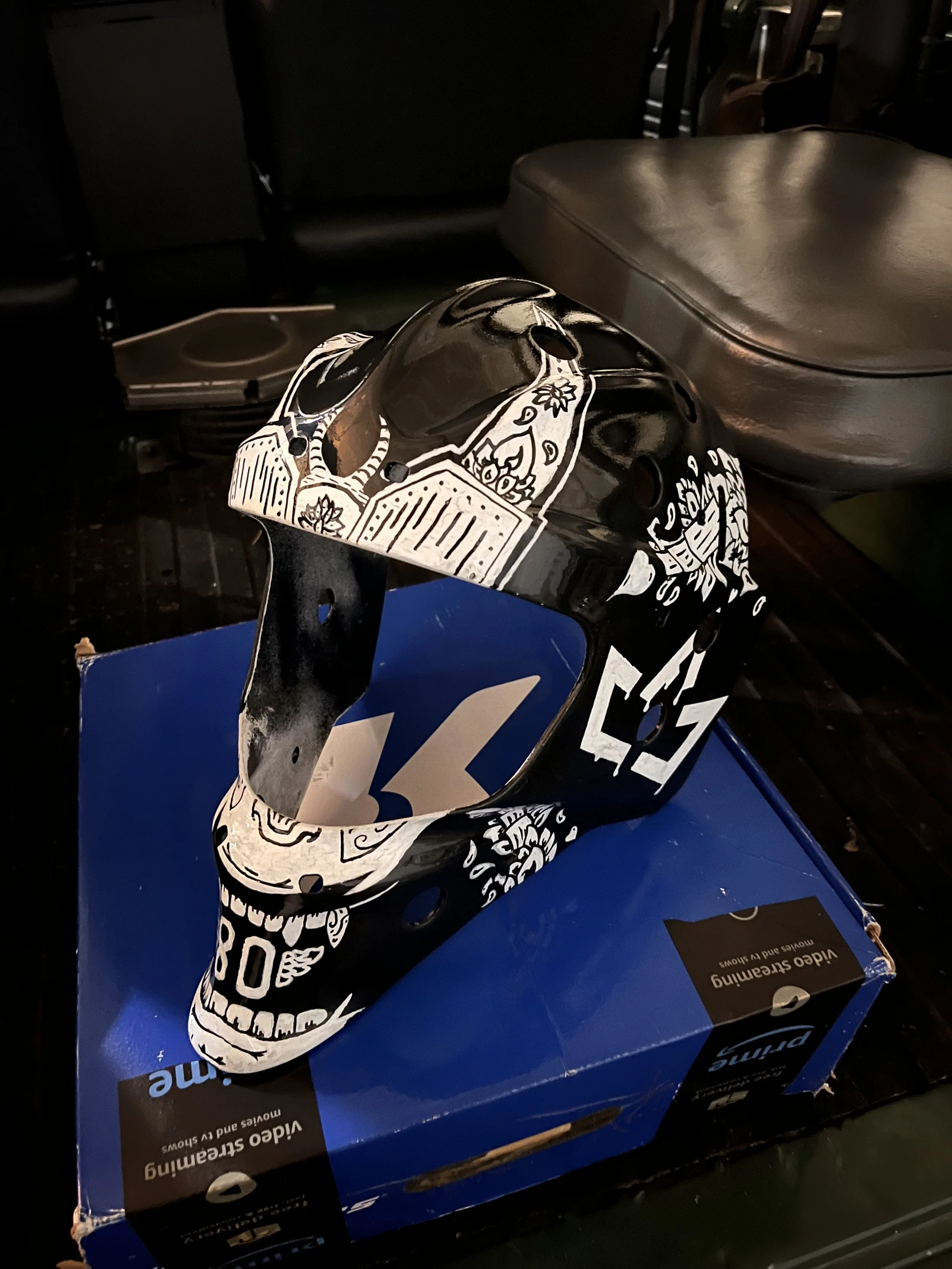 A cardboard box with a “Video Streaming Movies and Shows” label in front of a black motorcycle helmet with a black and white decorative design, placed on a blue box.