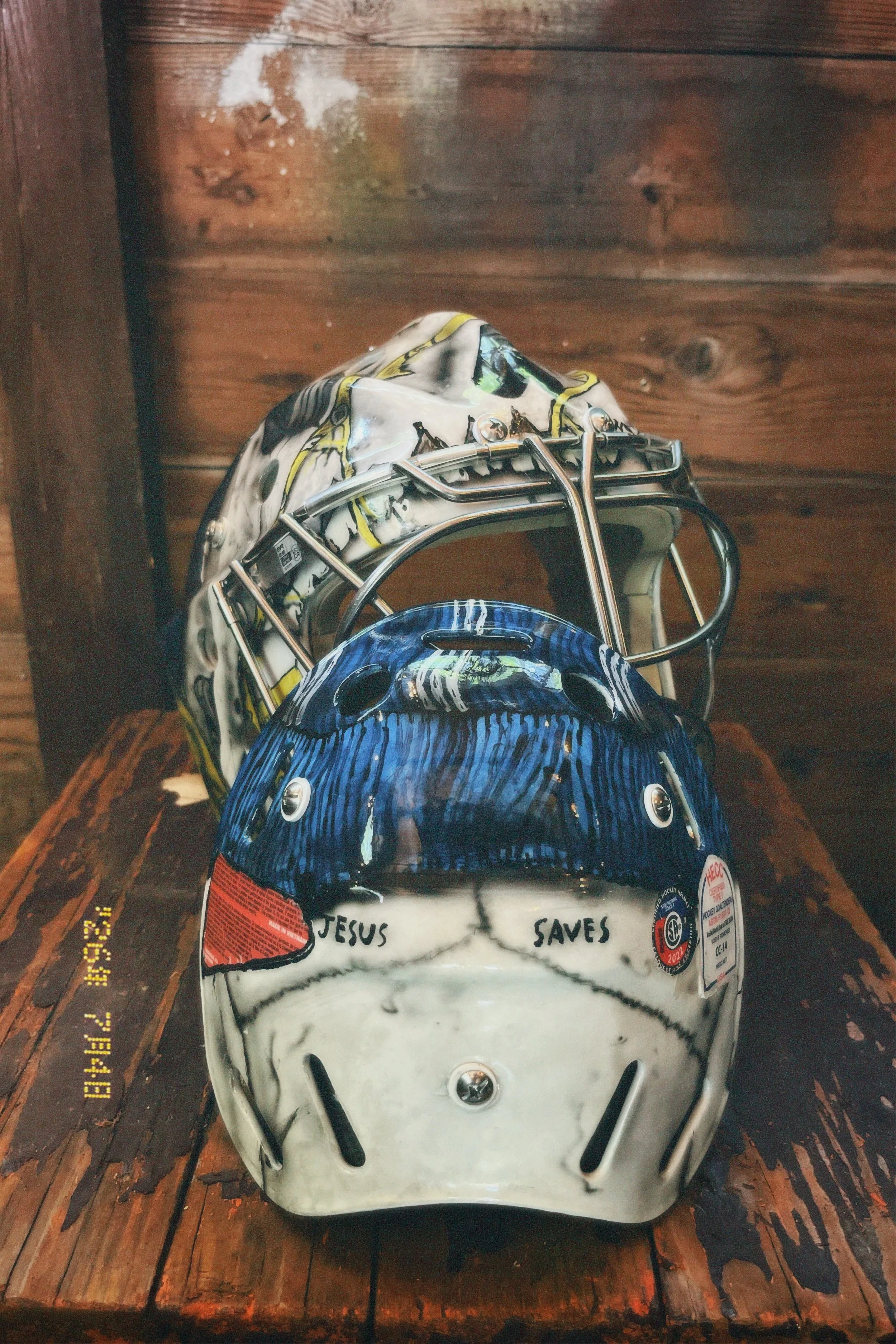 Ice hockey helmet with handwritten message 'JESUS SAVES' on the front, placed on a wooden surface.