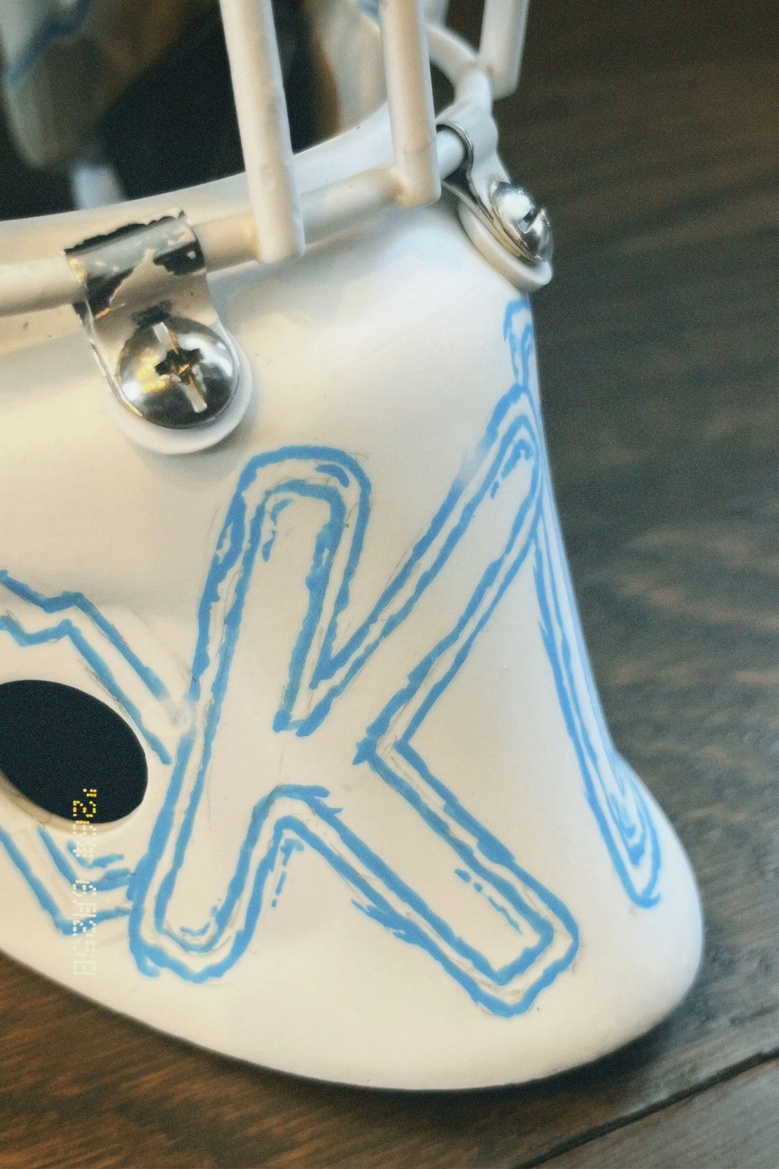 Close-up of a white object with blue line art design, metallic screws, and a small hole, resting on a wooden surface.