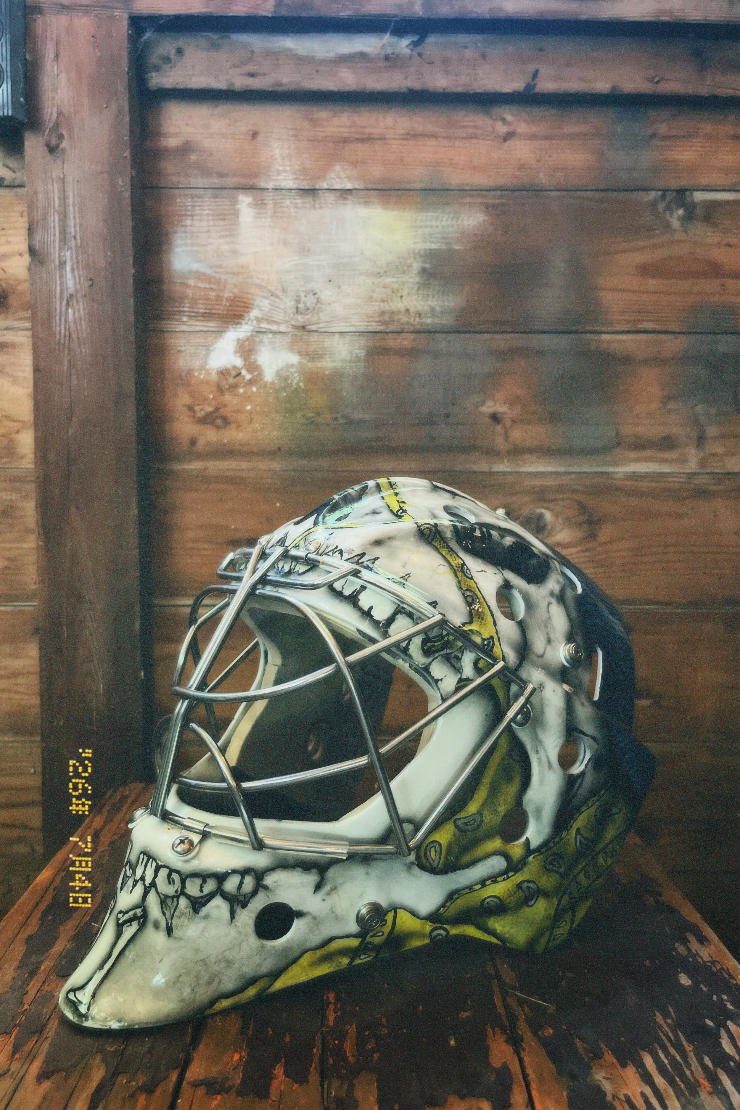 A helmet designed with a skull face in black and white with yellow accents, placed on a rustic wooden surface.