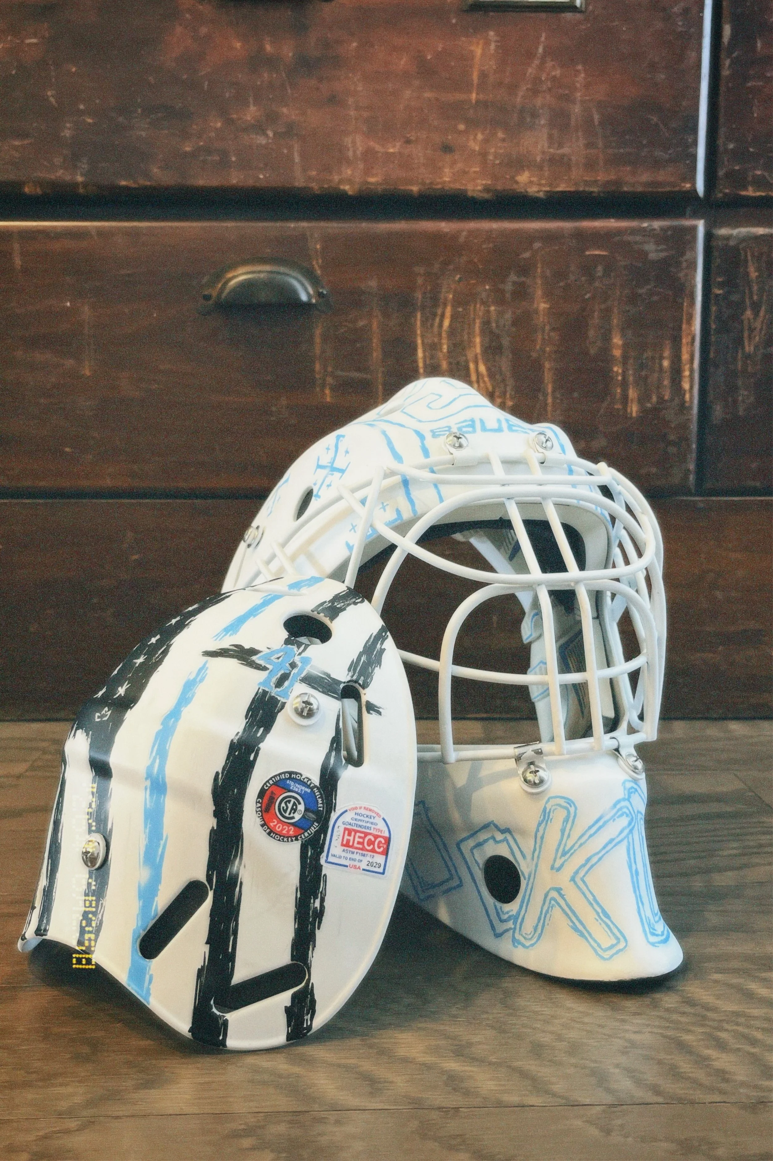 Ice hockey goal net with hockey puck, stickers, and markings, placed on wooden floor against dark wooden furniture.