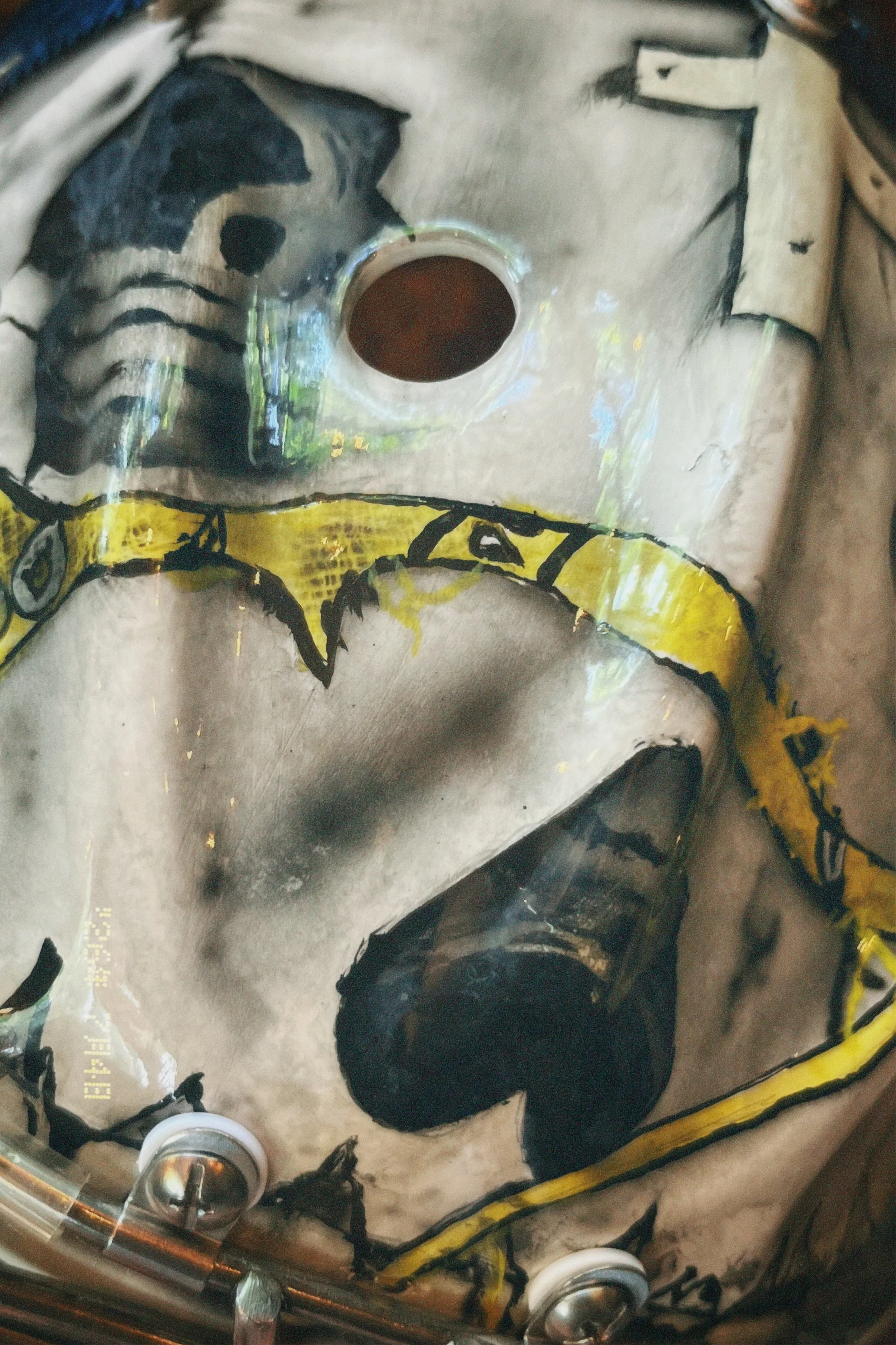 Close-up of a painted skull with black, yellow, and gray colors, and a dark hollow eye socket, on a metallic surface with reflective qualities.