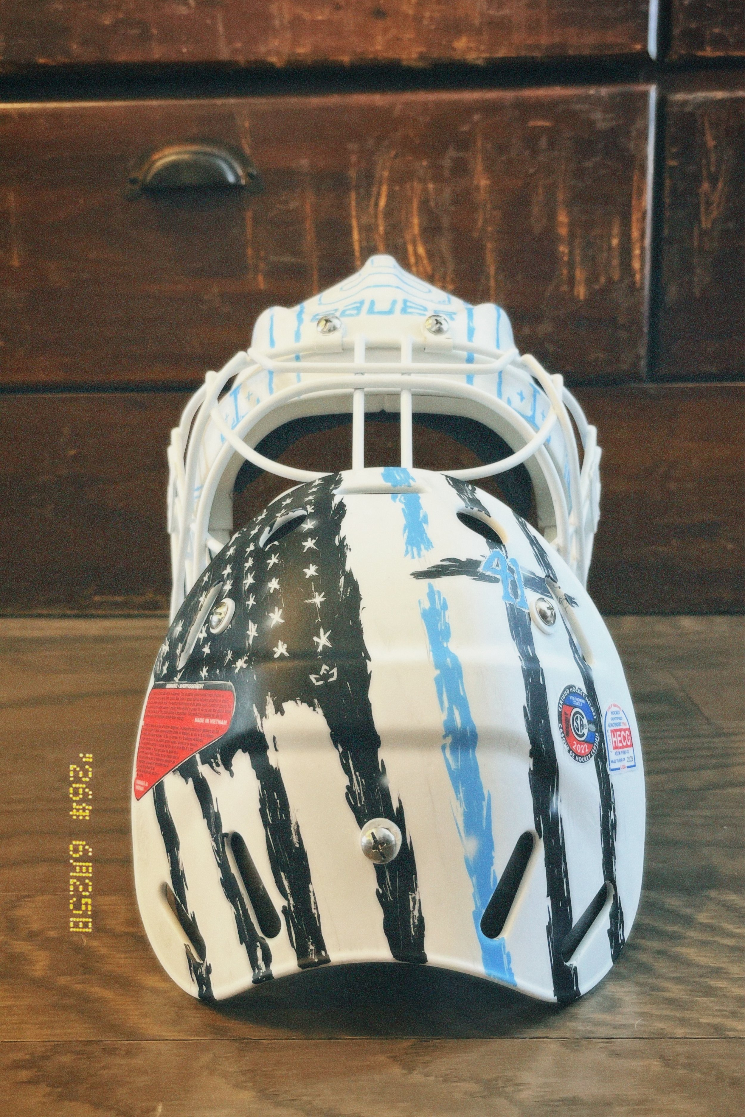 A hockey helmet with black, white, and blue graphics resting on a wooden surface.