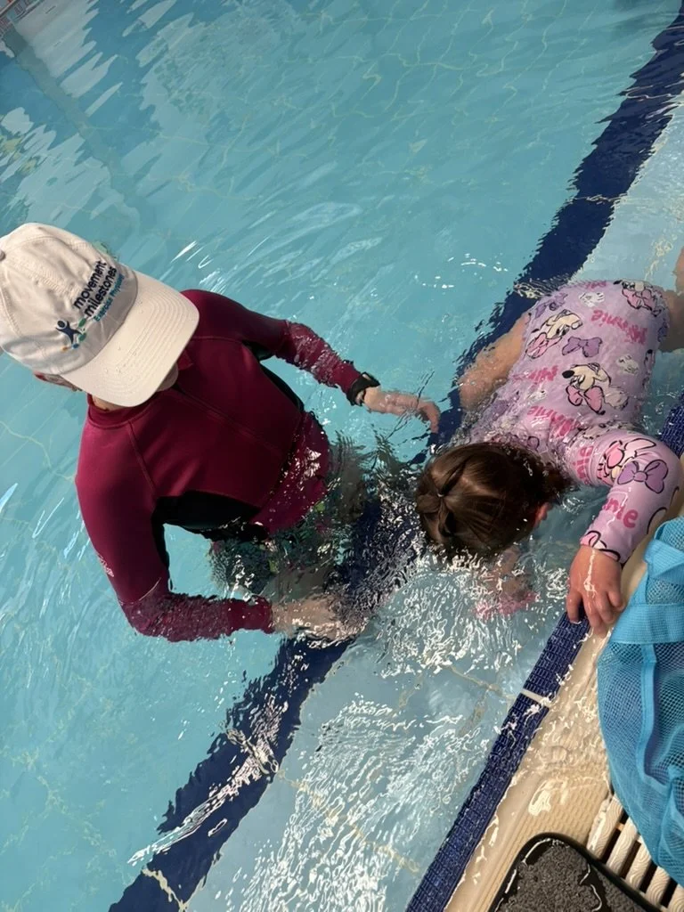 Adult assisting a young girl in learning to swim in a pool, with both holding onto the pool edge.