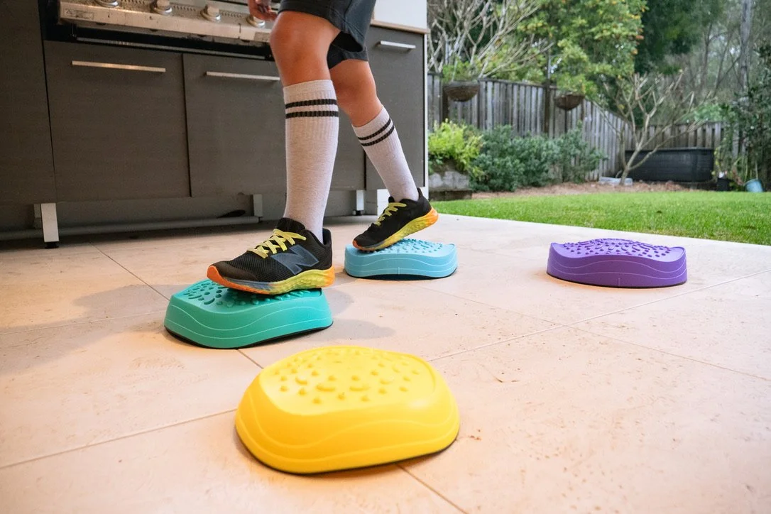 Person doing step exercises outdoors on colorful aerobic step platforms, wearing athletic shoes and knee-high striped socks.